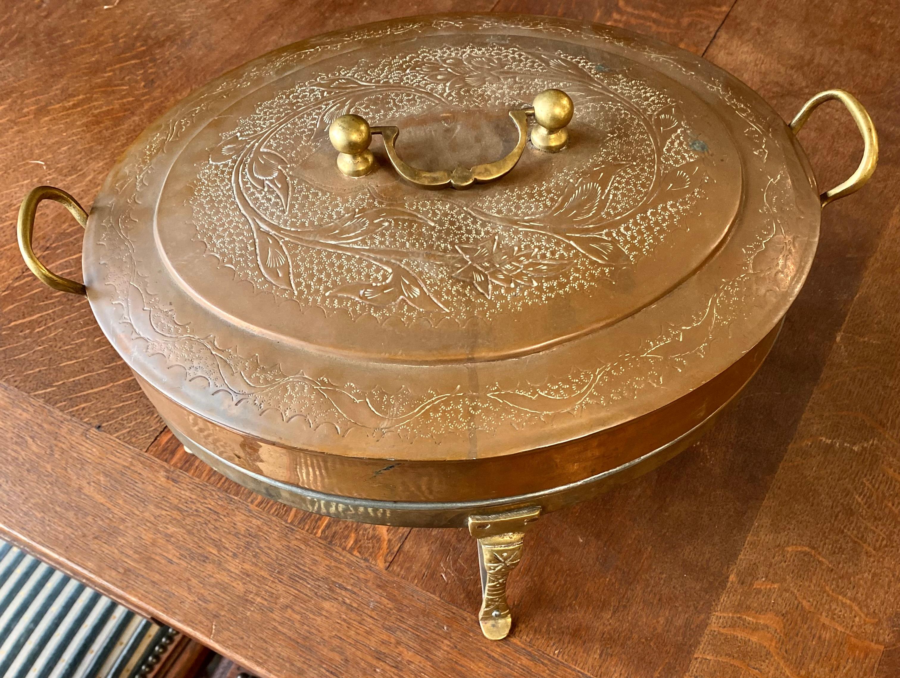 This vintage, large, oval beautifully engraved copper chaffing dish has solid brass handles on the sides and the top. There is a large cup for the sterno to sit in and the cabriole legs and feet are shaped nicely.
There is a large tin lined area for