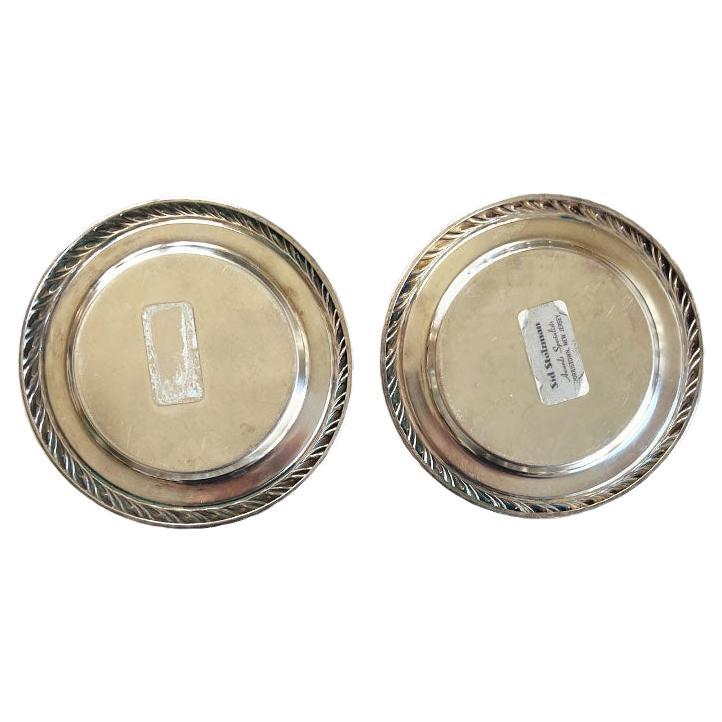 A pair of small round engraved silver plate trays by Oneida. Each plate is round with a lovely faux ribbon or rope detail around the edge. The center of each piece is engraved with 