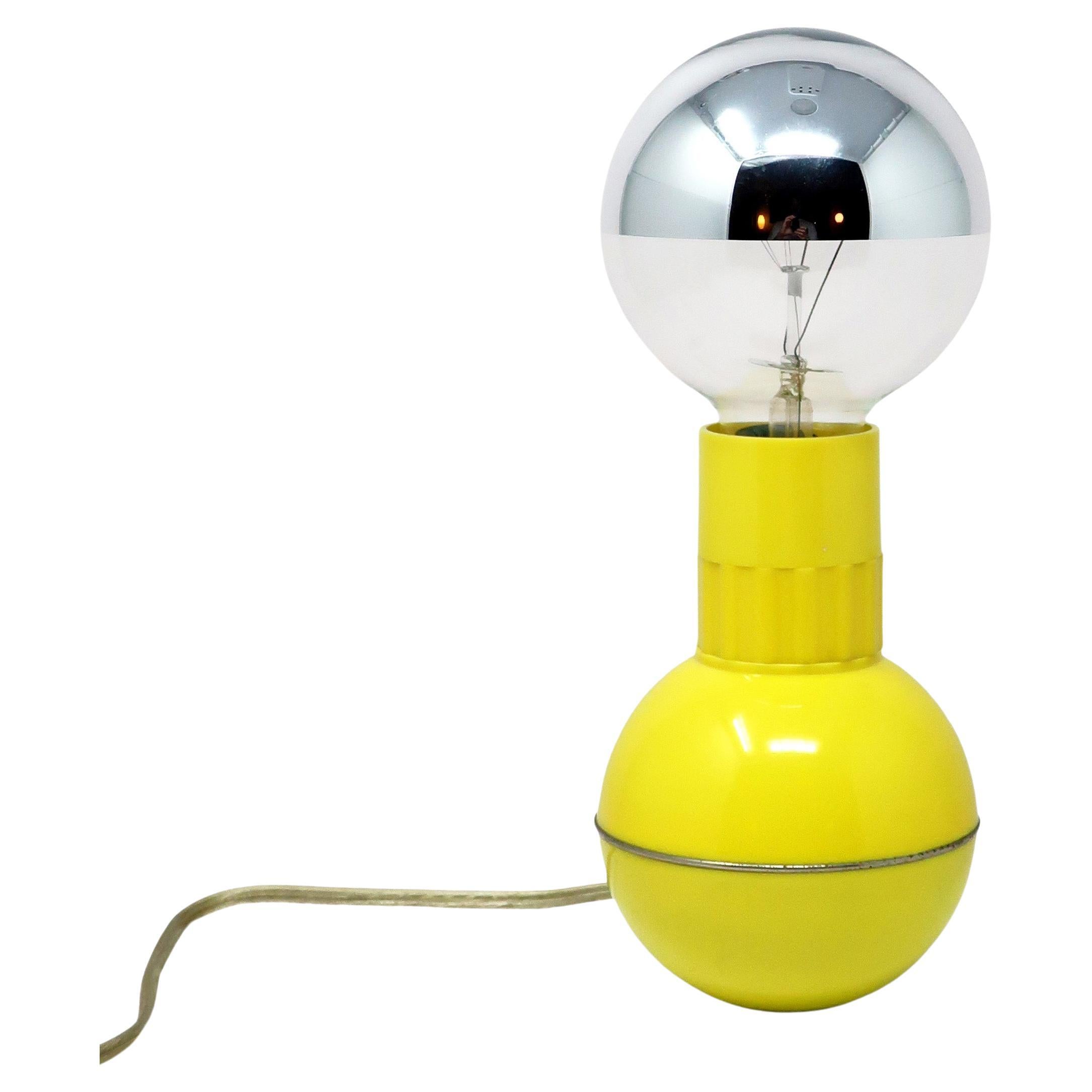 A classic by famed Italian design Enzo Mari that looks like a dumbbell.  Spherical weighted base with chrome ring keeps the lamp from tipping over, yellow ribbed collar turns on/off and dims the light, and half-dipped chrome bulb gives it a diffuse