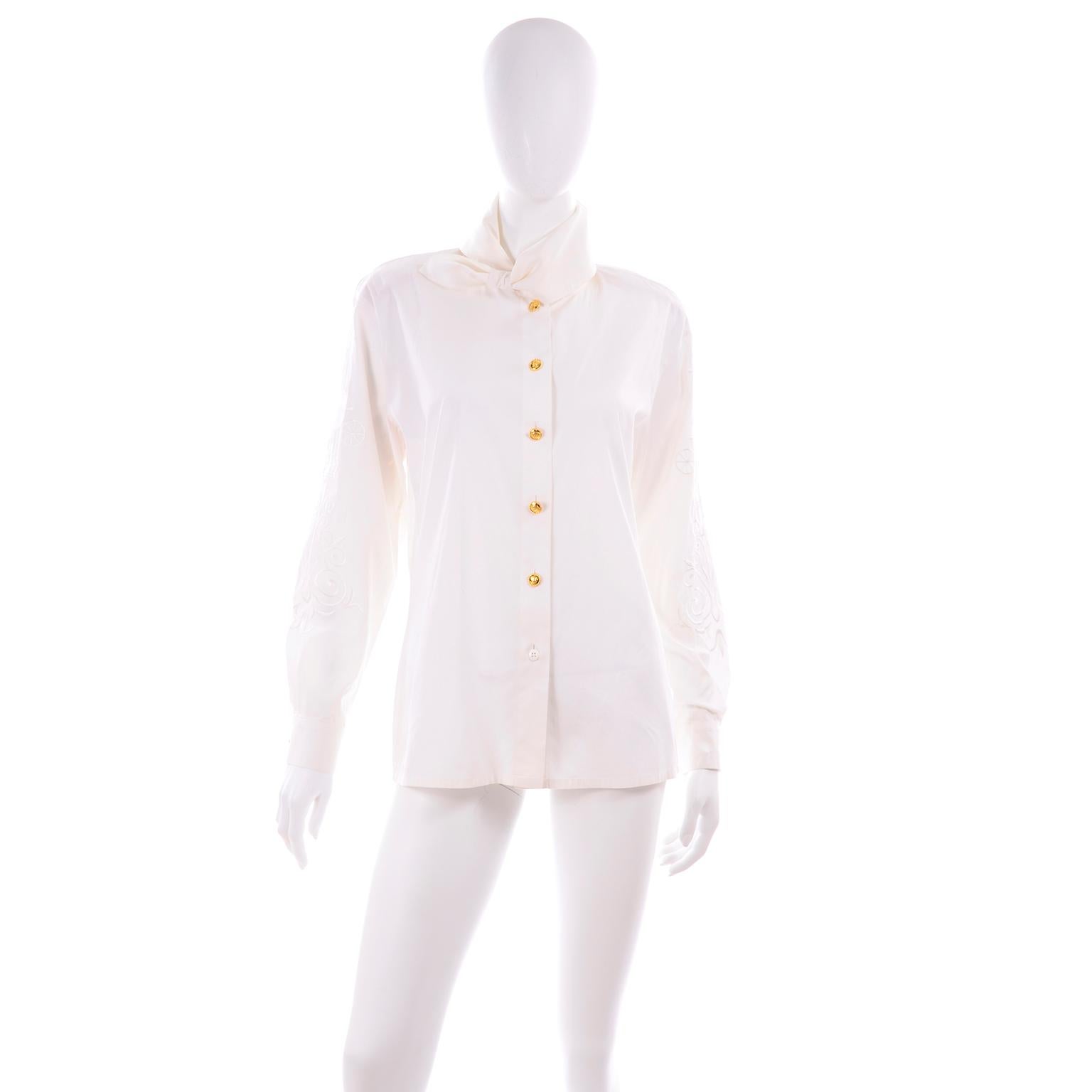 This is another great Escada vintage blouse designed by Margaretha Ley. This white cotton blouse features a scarf tie collar, embroidery on the sleeves that includes a carriage, a crown, and decorative flourishes. The beautiful gold buttons have