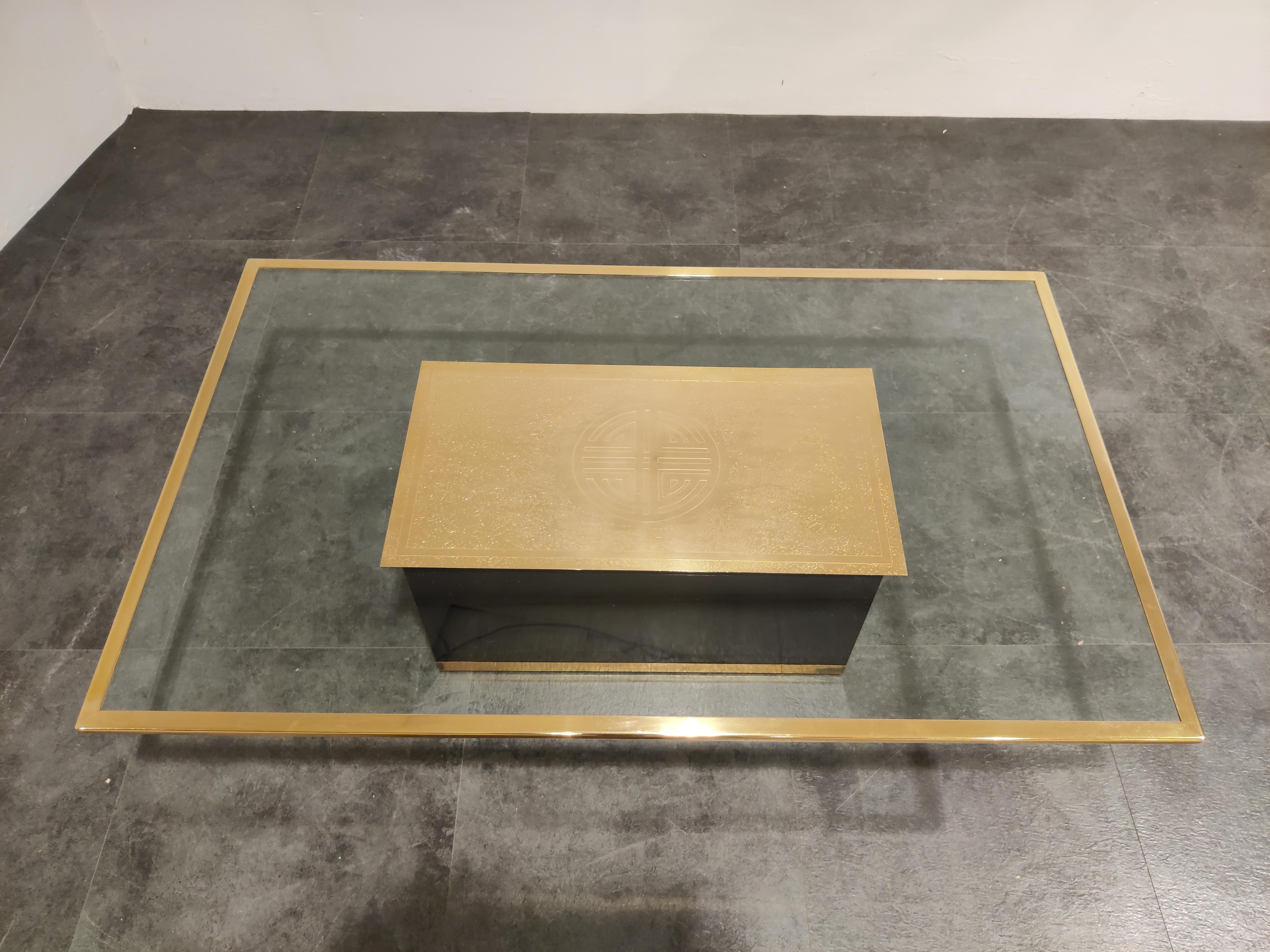 Table basse rectangulaire comprenant un plateau en verre transparent avec un bord en laiton monté sur une base en bois laqué noir avec une finition en laiton. 

La caractéristique principale de cette table basse est la plaque en laiton gravée