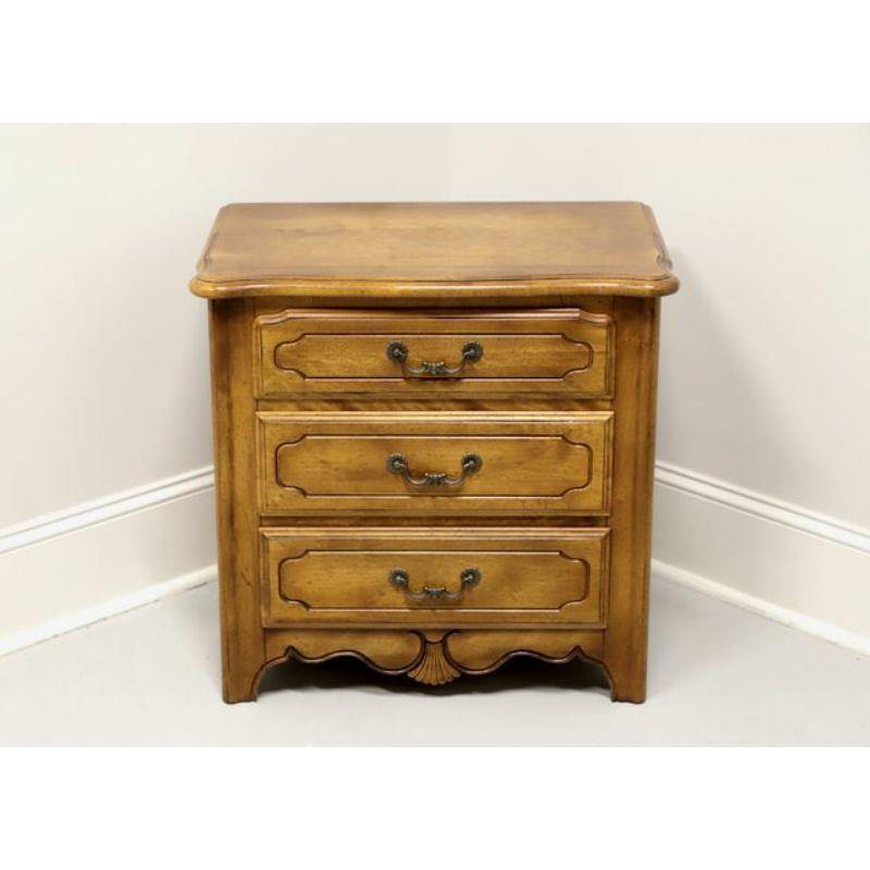 A nightstand in the French Country style by Ethan Allen. Walnut with a slightly distressed finish, serpentine top, decorative carved fan to apron and brass hardware. Features three drawers of dovetail construction. Made in the USA, circa