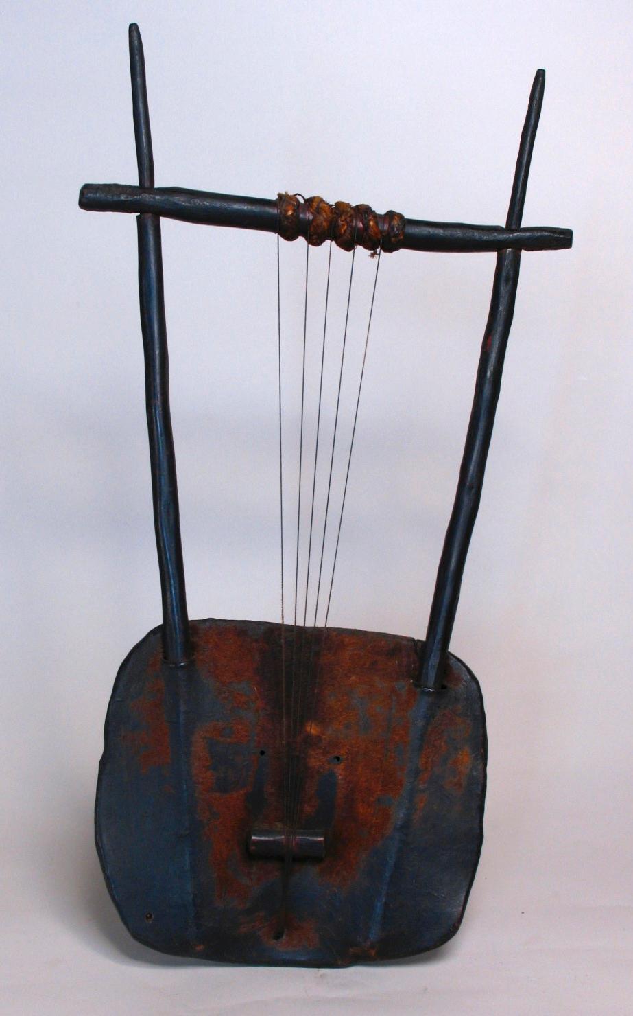 An Ethiopian dita, or krar, a five-string bowl-shaped lyre musical instrument, with a cowhide stretched tympanum over a wood squarish bowl base and wood uprights and cross member.
Measures: 28” high x 15” wide x 3” deep.
Minor signs of age and