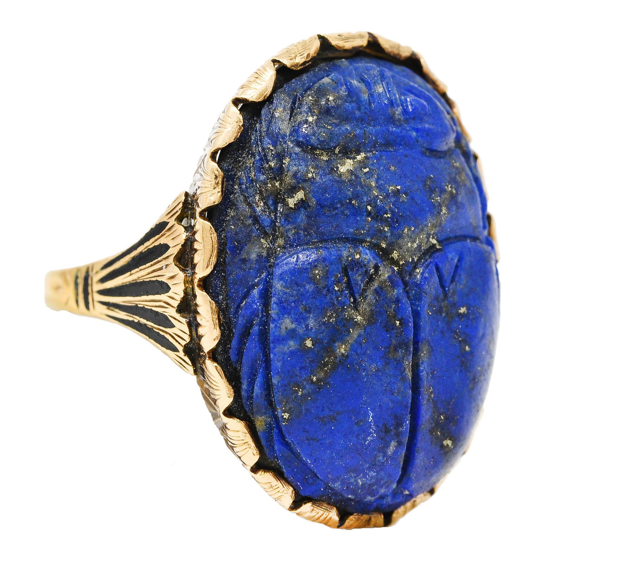 Centering a 17.0 x 22.0 mm oval lapis lazuli cabochon - carved to depict a scarab beetle. Opaque ultramarine blue with pyrite flecking - set in a stylized scalloped bezel. With foliate engraved basket fully around. With grooved fanning shoulders.