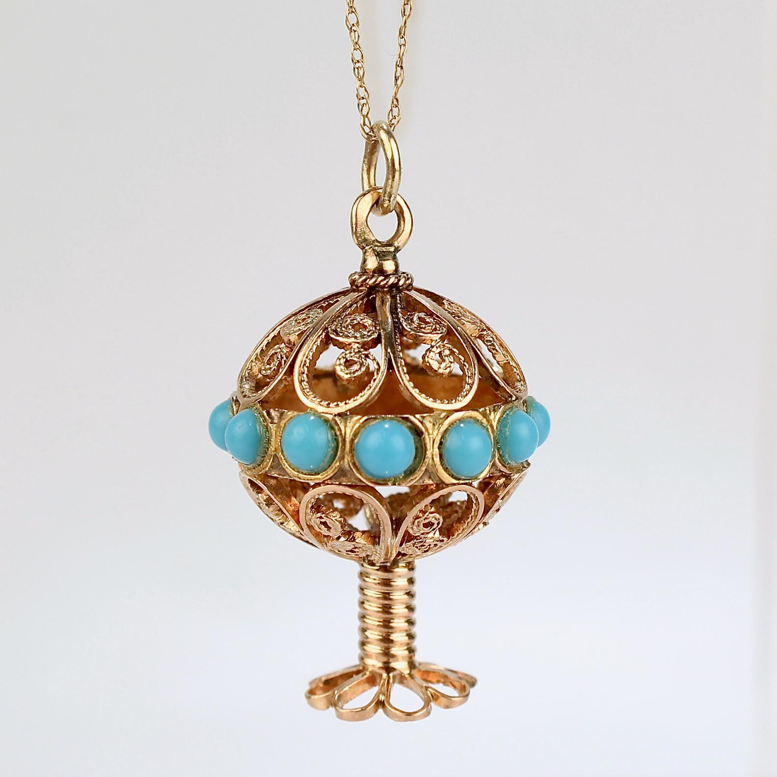 A very fine gold Etruscan Revival pendant charm.

In 18k yellow gold.

In the form of a hollow sphere with filigree flower petal sections and smooth round turquoise cabochons set around a center sphere that is supported by a gold coil pedestal and