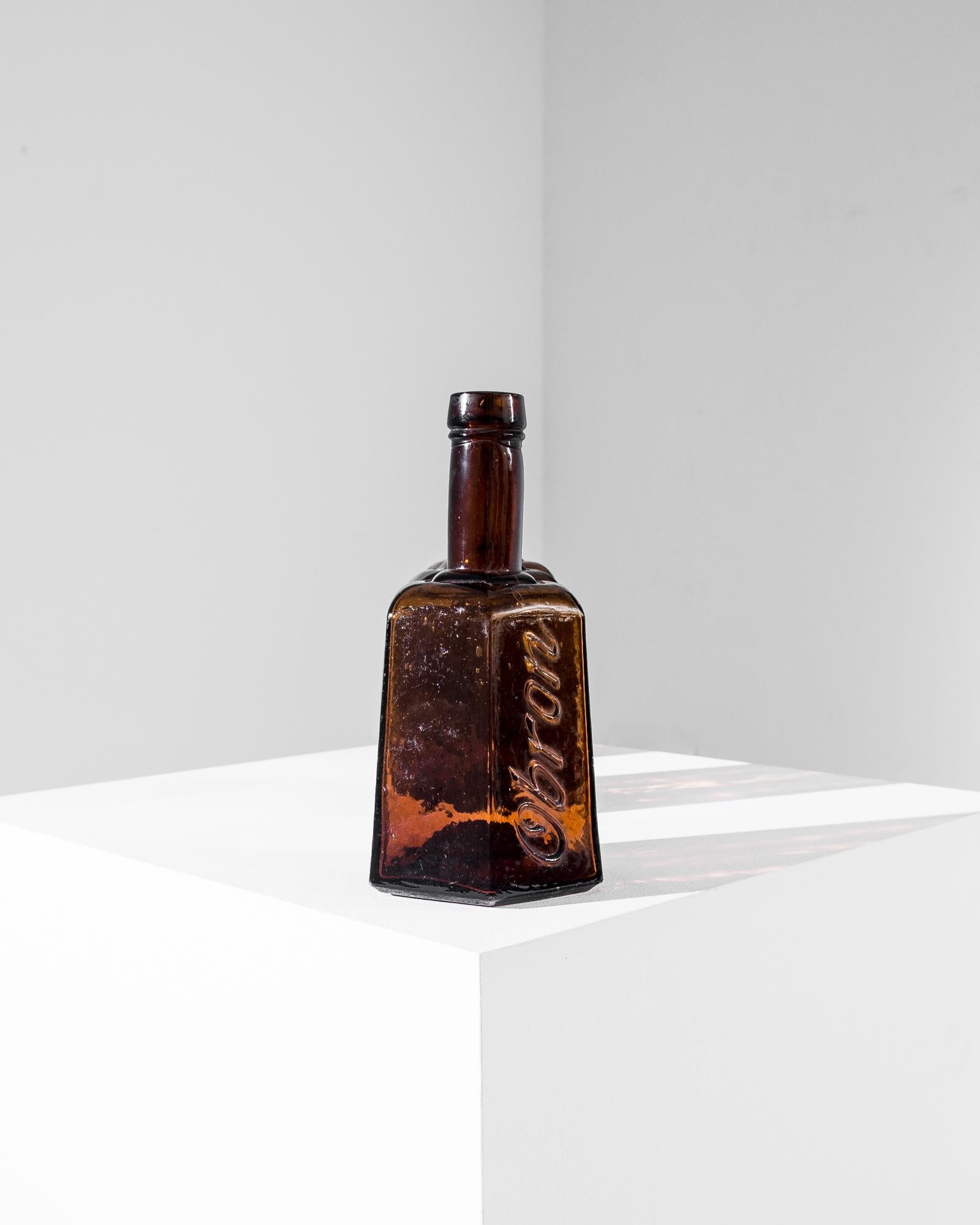 A vintage glass bottle from Europe, produced around 1900. Originally containing concentrated bouillon, the charming bottles were too beautiful to let go. Thick, light brown glass forms a hexagonal body embossed with the brand “Obron” under a long,