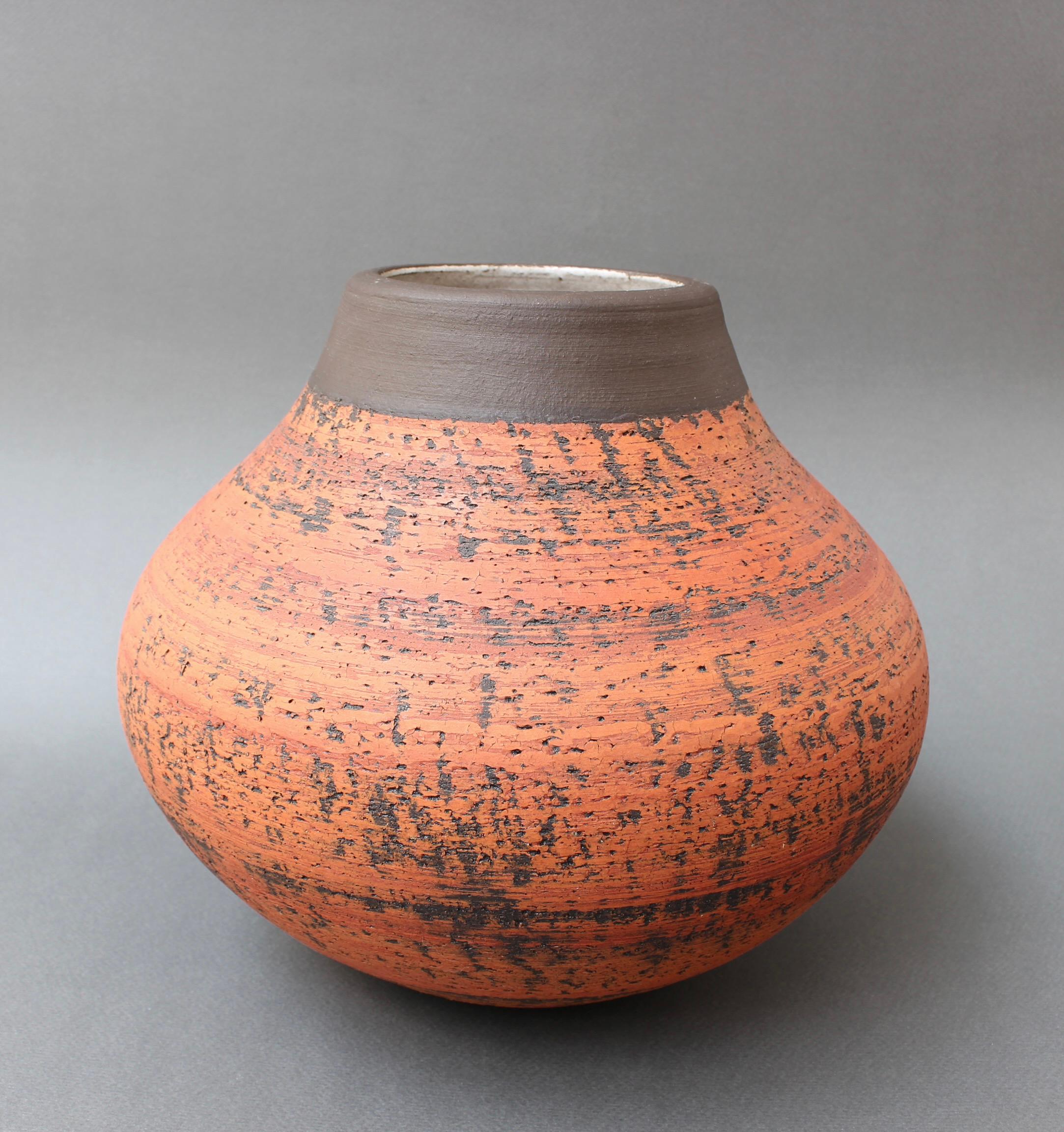 Vintage European earthenware vase (circa 1970s). A very rustic piece with a matt orange hue accented by incised brown markings encircling the body. The same colour encircles the neck and lip but provides tactile contrast with its even feel and more