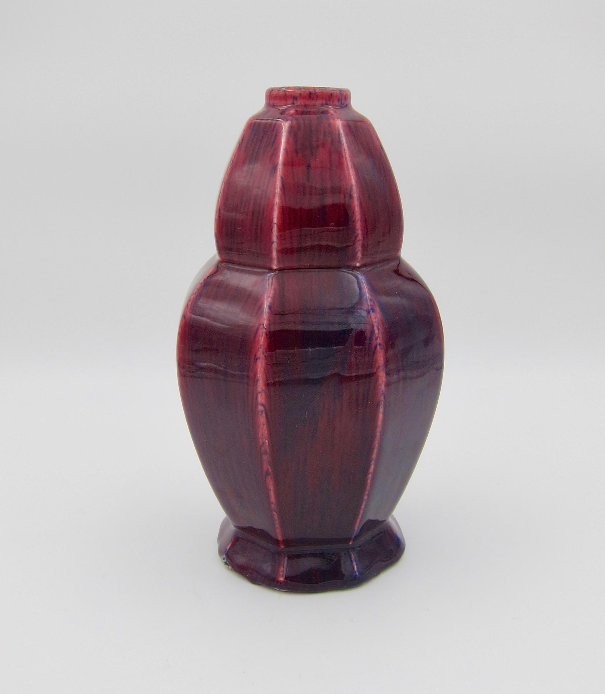 A vintage European art pottery vase in an octagonal Art Deco shape enveloped in a deep pink/red glaze with dark blue hand painted accents. At a distance, the colors combine to create the appearance of a glossy oxblood-colored glaze. The earthenware
