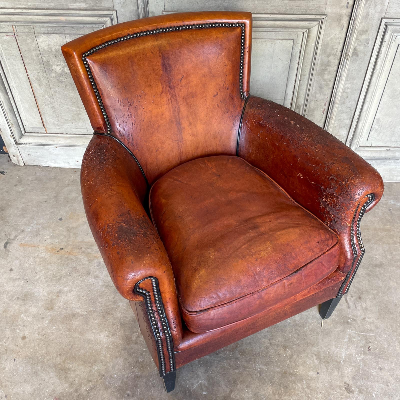 This vintage European leather club chair features richly patinated leather and brass nailhead detail. The feet are wood and slightly tapered. The style of this armchair is perfect for floating in a space or tucked in a corner, as it's beautiful from