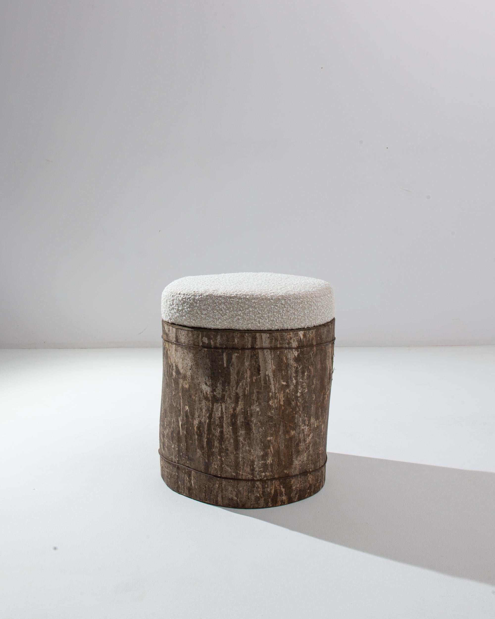 A wooden and upholstered ottoman from 19th century Central Europe. This refreshingly minimal stool is composed of a thick cut of tree trunk wrapped in wire and topped with fresh boucle reupholstery. Providing both a refined elegance and a breath of