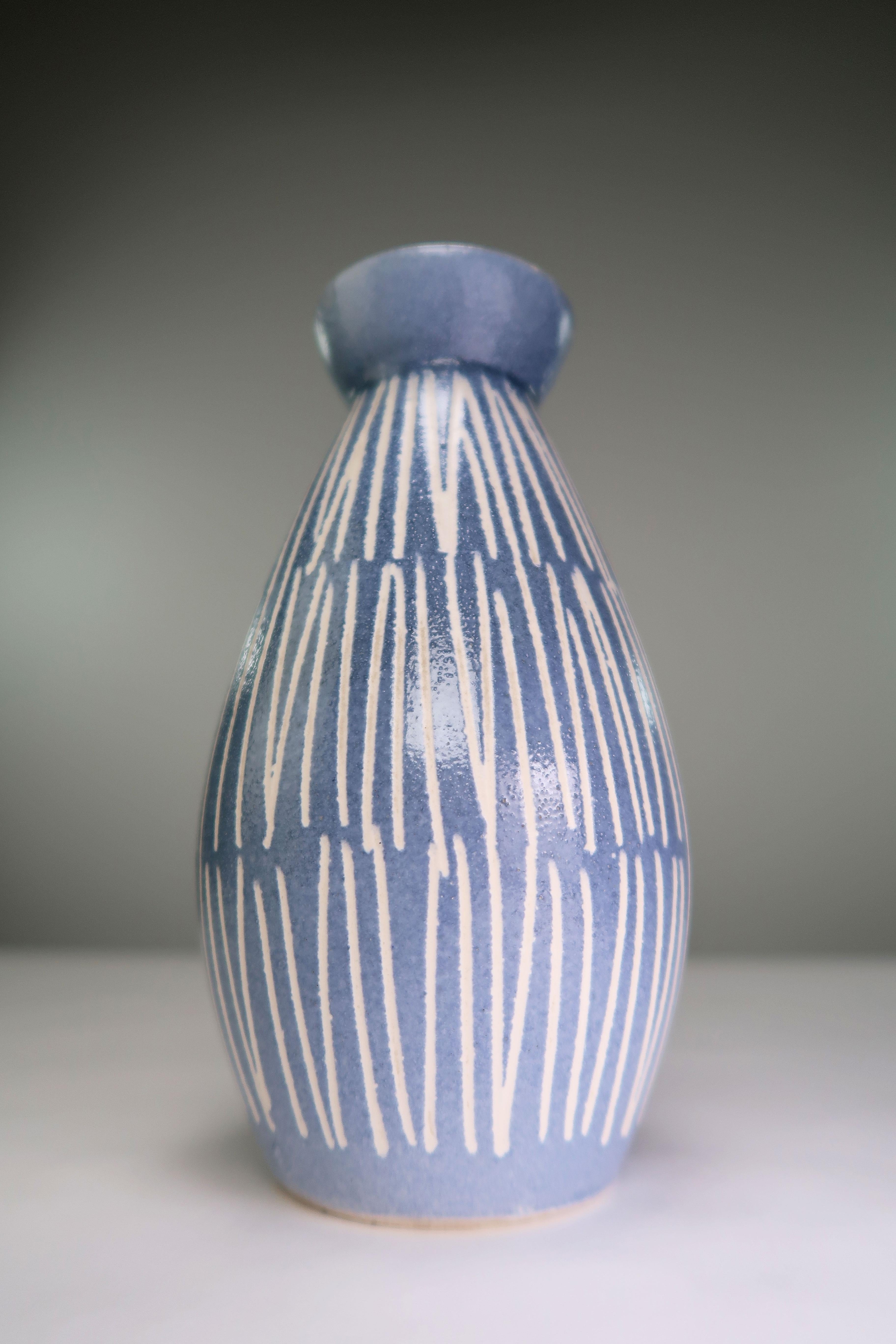 Schöne und lebendige hellblaue Vintage-Vase aus der Mitte der 1960er-Jahre. Ausgeprägte schlanke und präzise weiße Streifen auf hellblauem Grund mit glasierter Innenseite in Schwarz und Grün um die oberen Kanten. Unter dem Sockel signiert. In