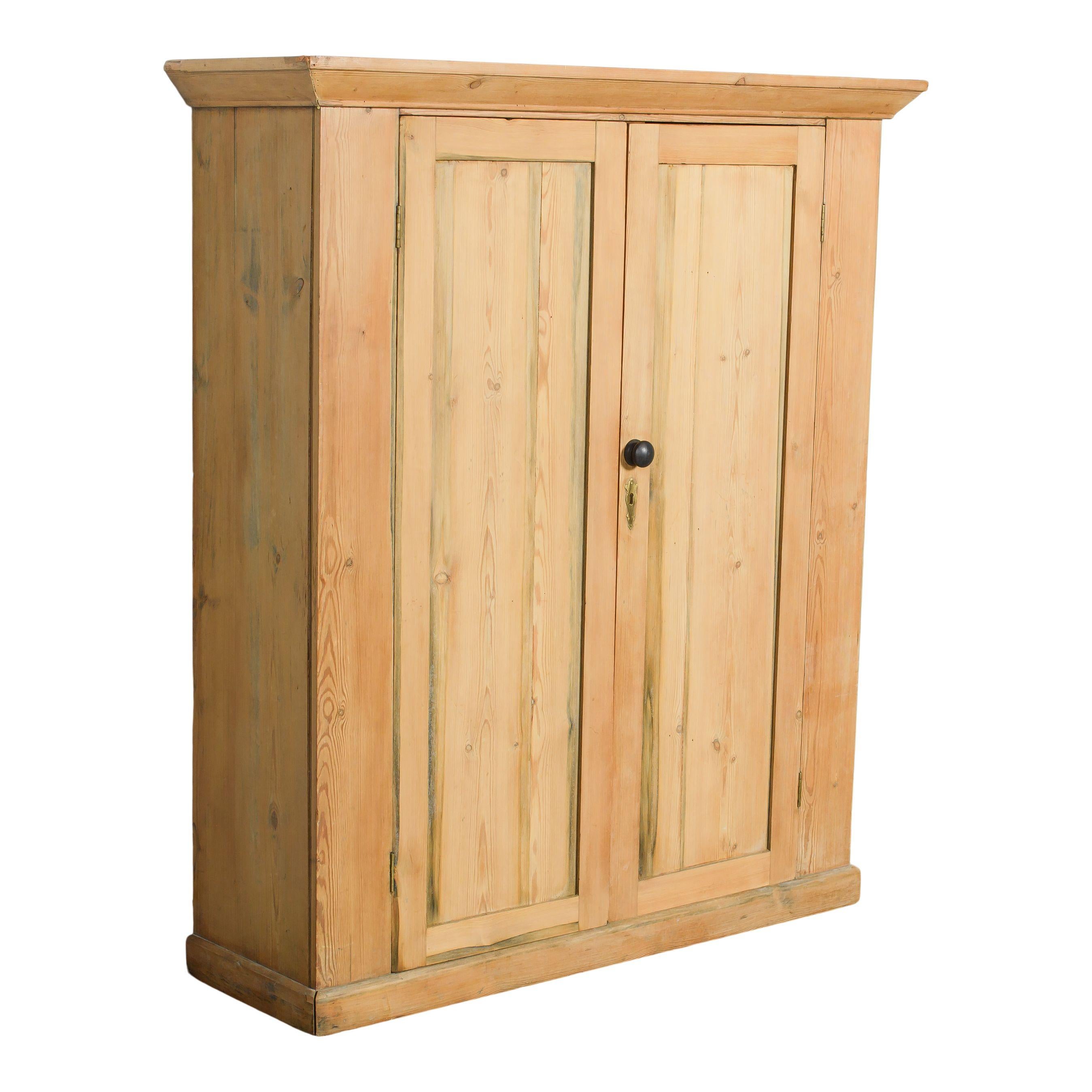 Une armoire en bois vintage d'Europe. Le bois est brut et s'estompe après des années d'utilisation, ce qui donne à la pièce une ambiance vintage douce et charmante. Cette armoire présente un design rectangulaire simple et deux grandes portes qui