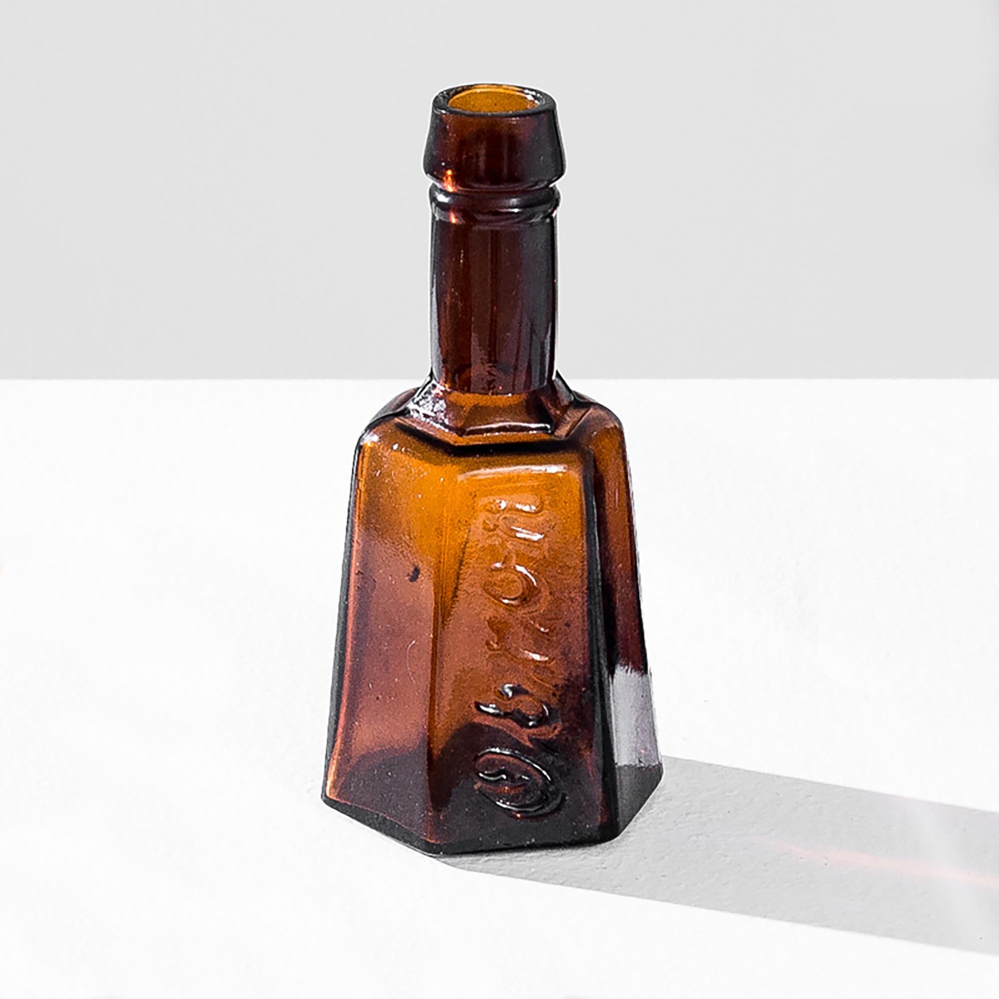 A vintage glass bottle from Europe, produced around 1900. Originally containing concentrated bouillon, the charming bottles were too beautiful to let go. Thick, light brown glass forms a hexagonal body embossed with the brand “Obron” under a long,