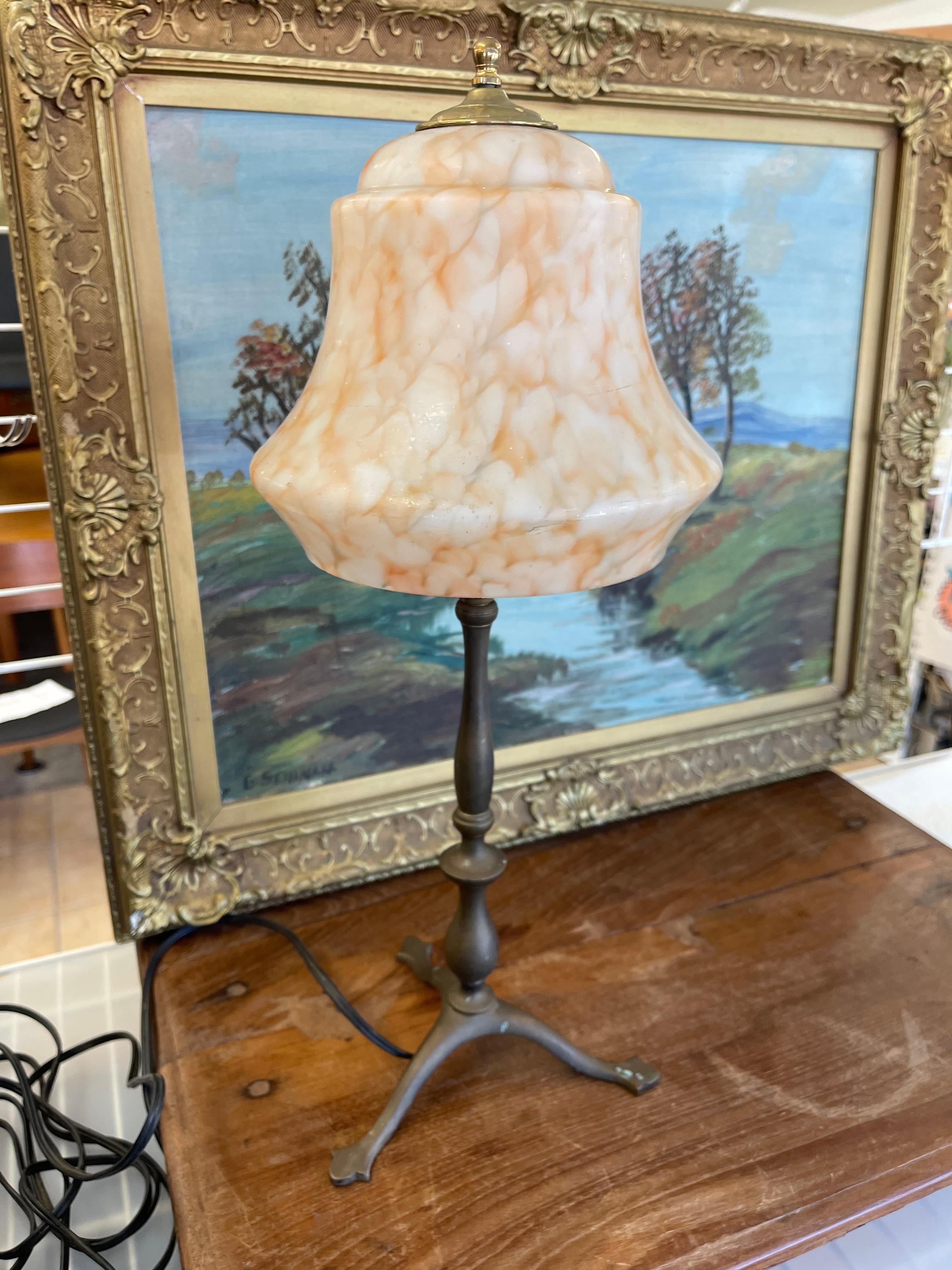  Cette lampe de table européenne vintage présente une base en métal sculpté avec un design à trois pieds et un abat-jour en verre tourbillonnant dans des tons chauds de crème et d'orange. L'abat-jour en verre en forme de cloche présente un motif