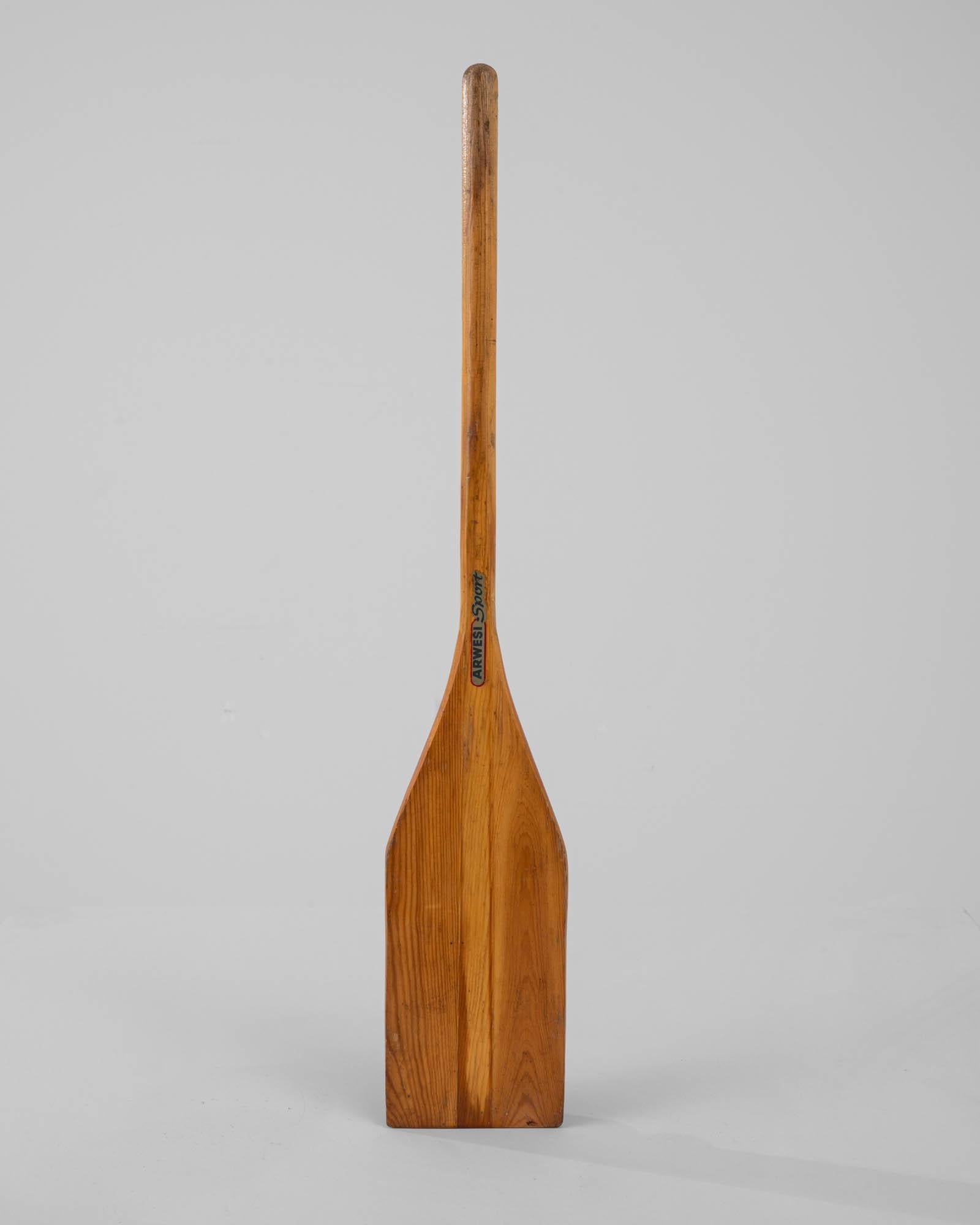 This wooden boat oar was made in 20th Century Germany. The polished wood has a smooth finish with a light multi-toned auburn brown shaft. Perfect for hanging on the wall, oars will complete a beach house or impart the charm of an idyllic lake to any