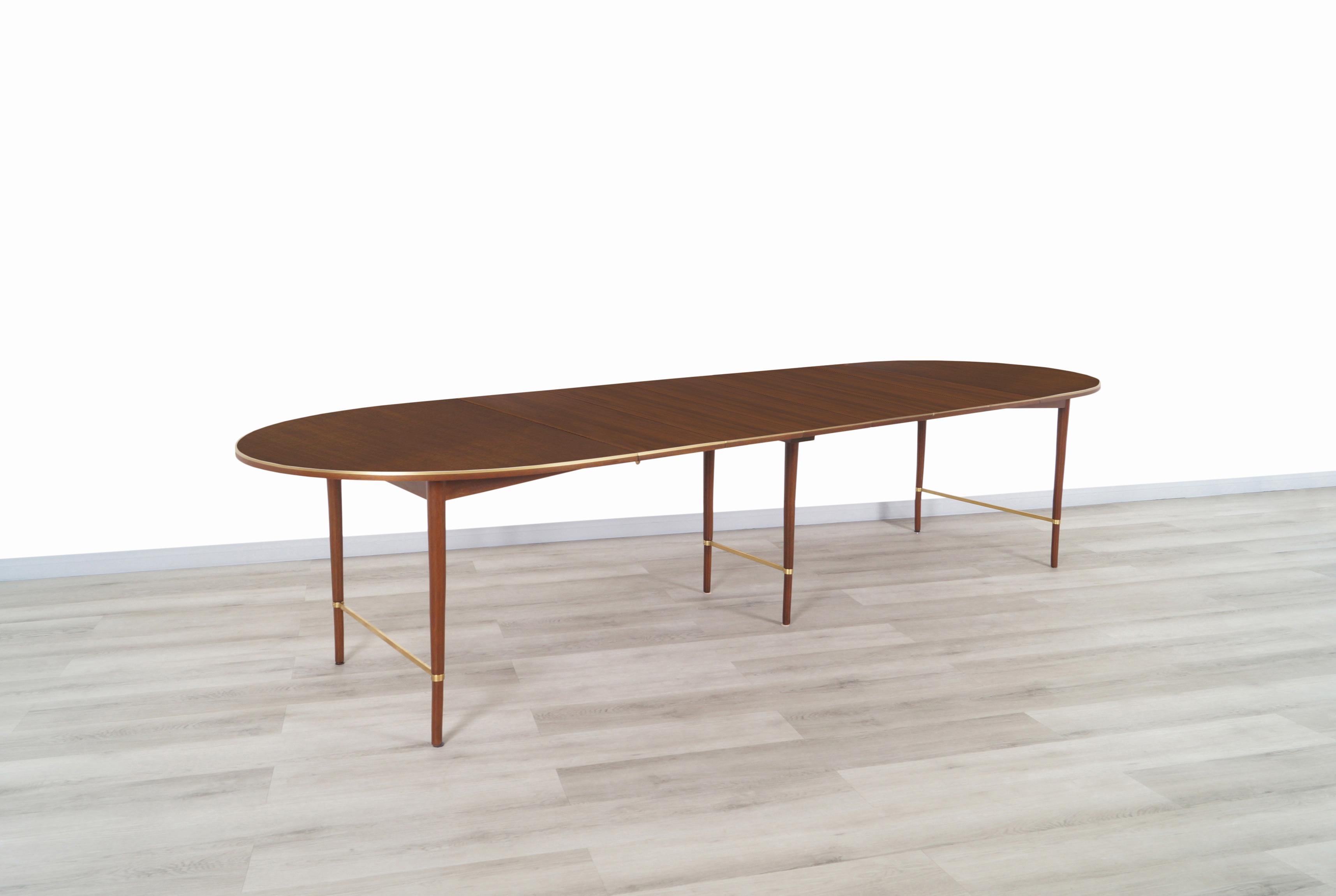 A beautiful vintage expanding dining table designed by Paul McCobb for H. Sacks & Son as part of the Connoisseur Collection. An excellent design that shows the quality craftsmanship of Paul McCobb. This table features an oval walnut top with lovely