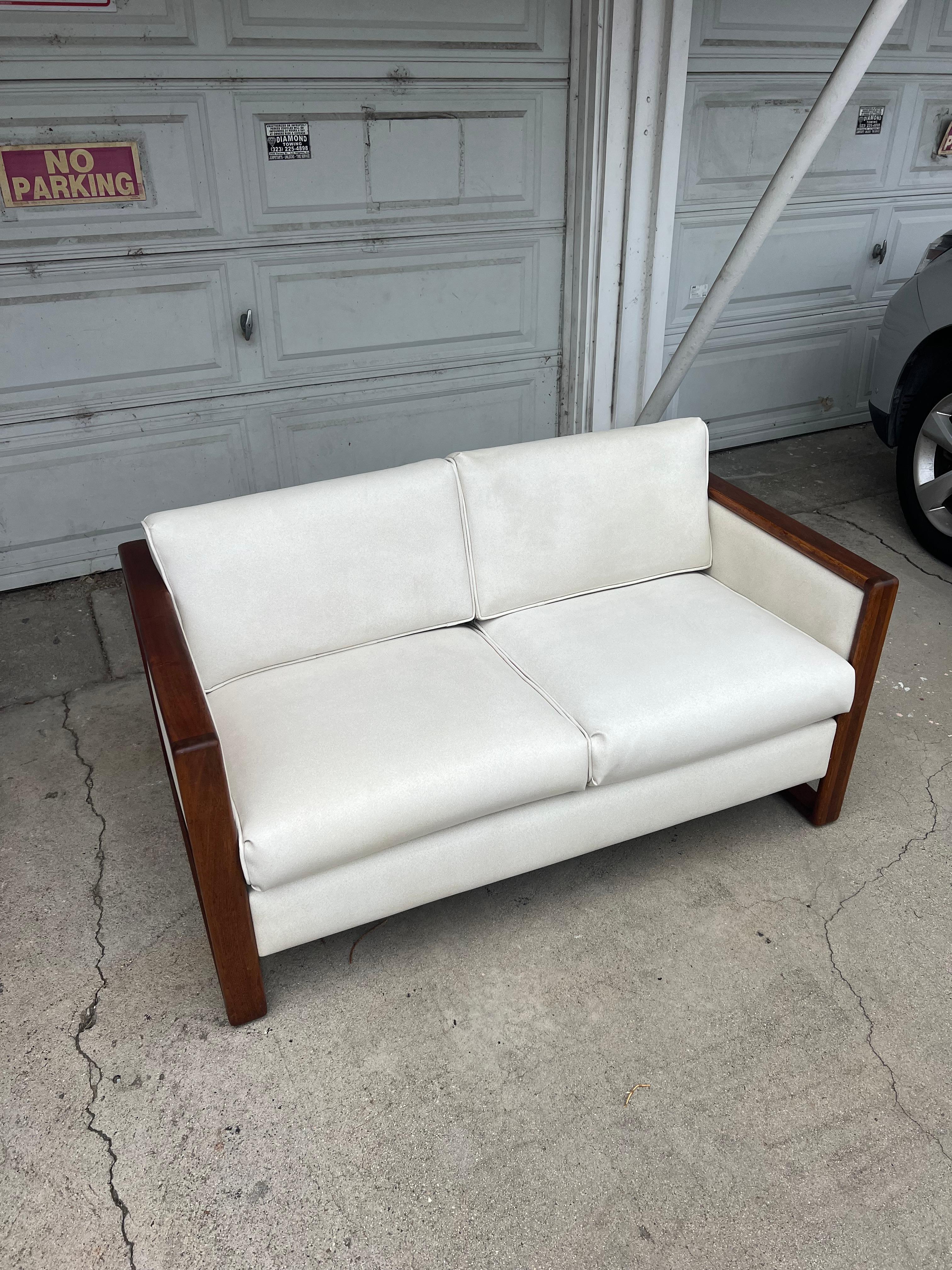 Super special vintage loveseat hailing from the 1970s with original upholstery in ivory speckled vinyl. Seat cushions attach to hook at crease between seat and back while seat back pillows rest atop to create a comfortable and attractive loveseat.