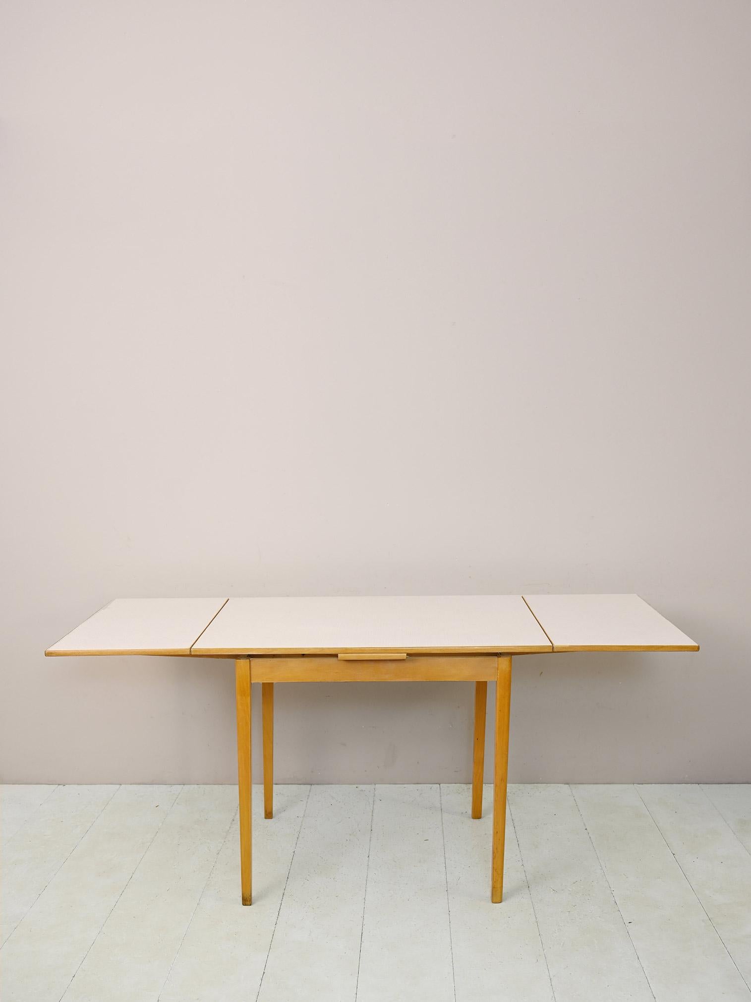 1960s dining table.

An iconic piece of mid-century design. The formica top can be extended on both sides thanks to the presence of the pull-out wings. 
The light birch wood frame and simple, square lines make it a piece of furniture suitable for