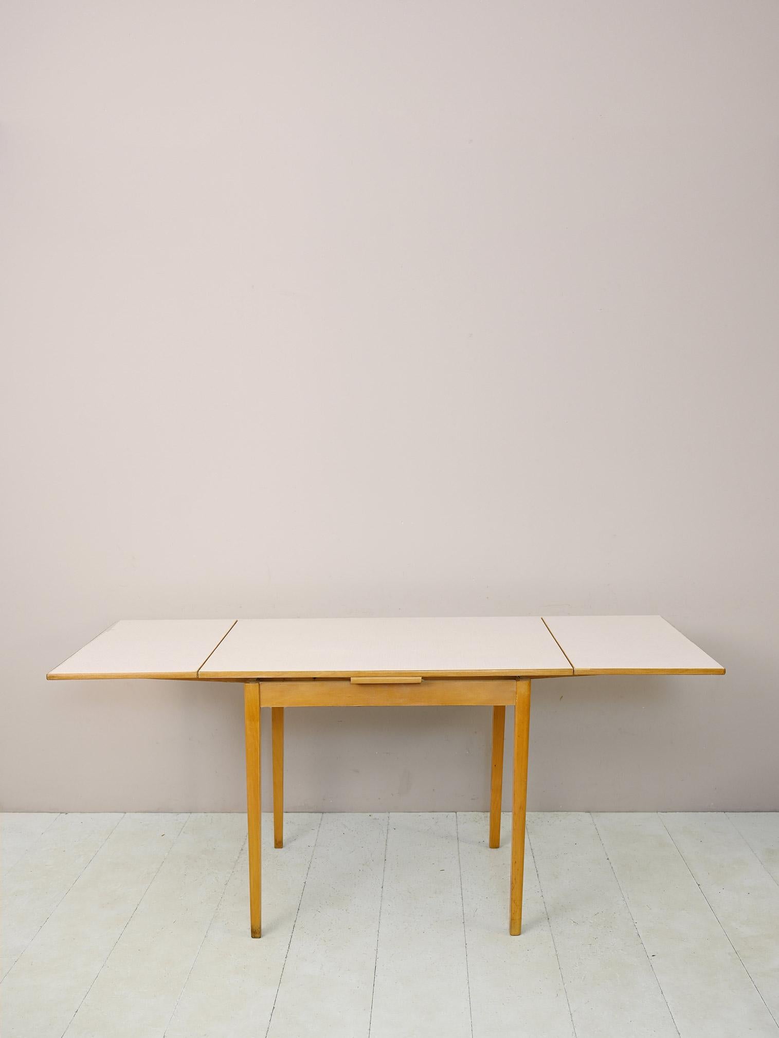 Table de salle à manger des années 1960.

Une pièce emblématique du design du milieu du siècle. Le plateau en formica peut être prolongé des deux côtés grâce à la présence des ailes extractibles. 
Le cadre en bois de bouleau clair et les lignes
