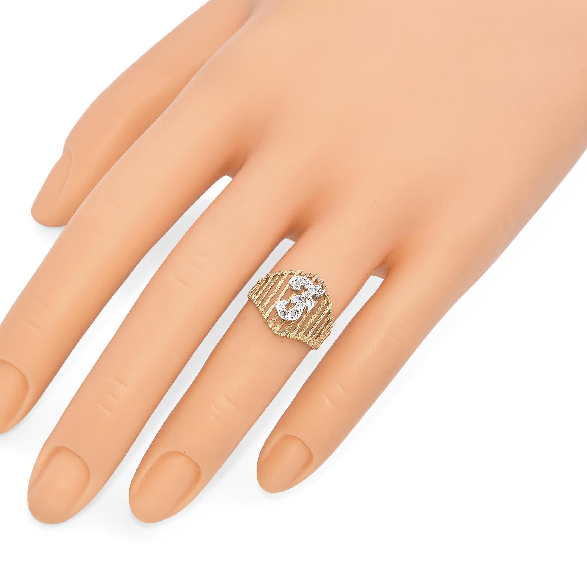 This striking ring features a textured gold band with vertical bars, creating an openwork design. At the center, a bold silver initial 