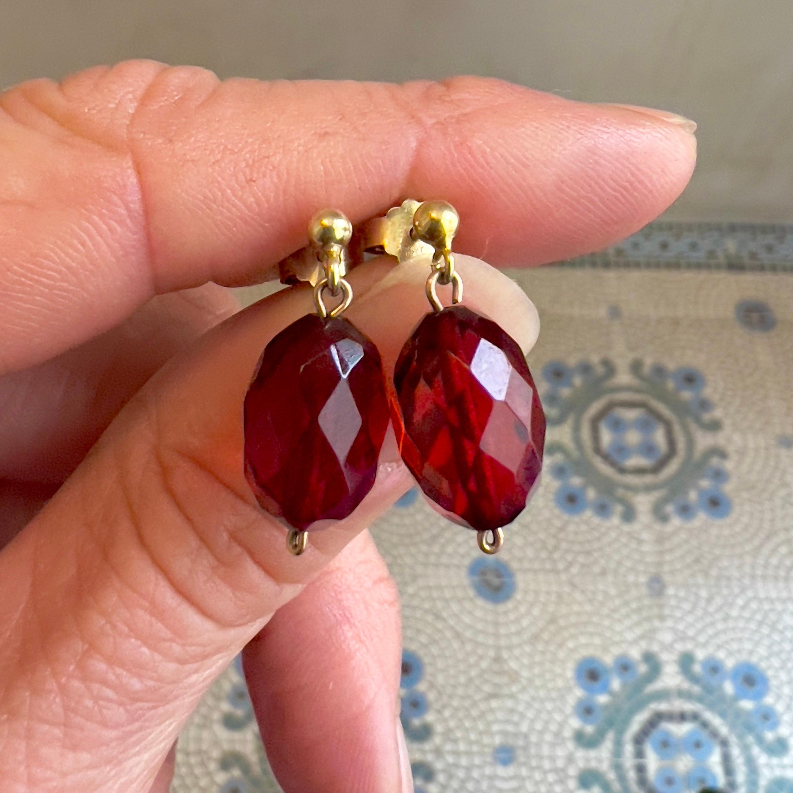 This pair of vintage earrings features vibrant faceted red amber stones in an elegant oval grape shape, set in a classic 14 karat gold ear pieces added for luxury and comfort. The oval-shaped red amber colored stones catches the light beautifully,