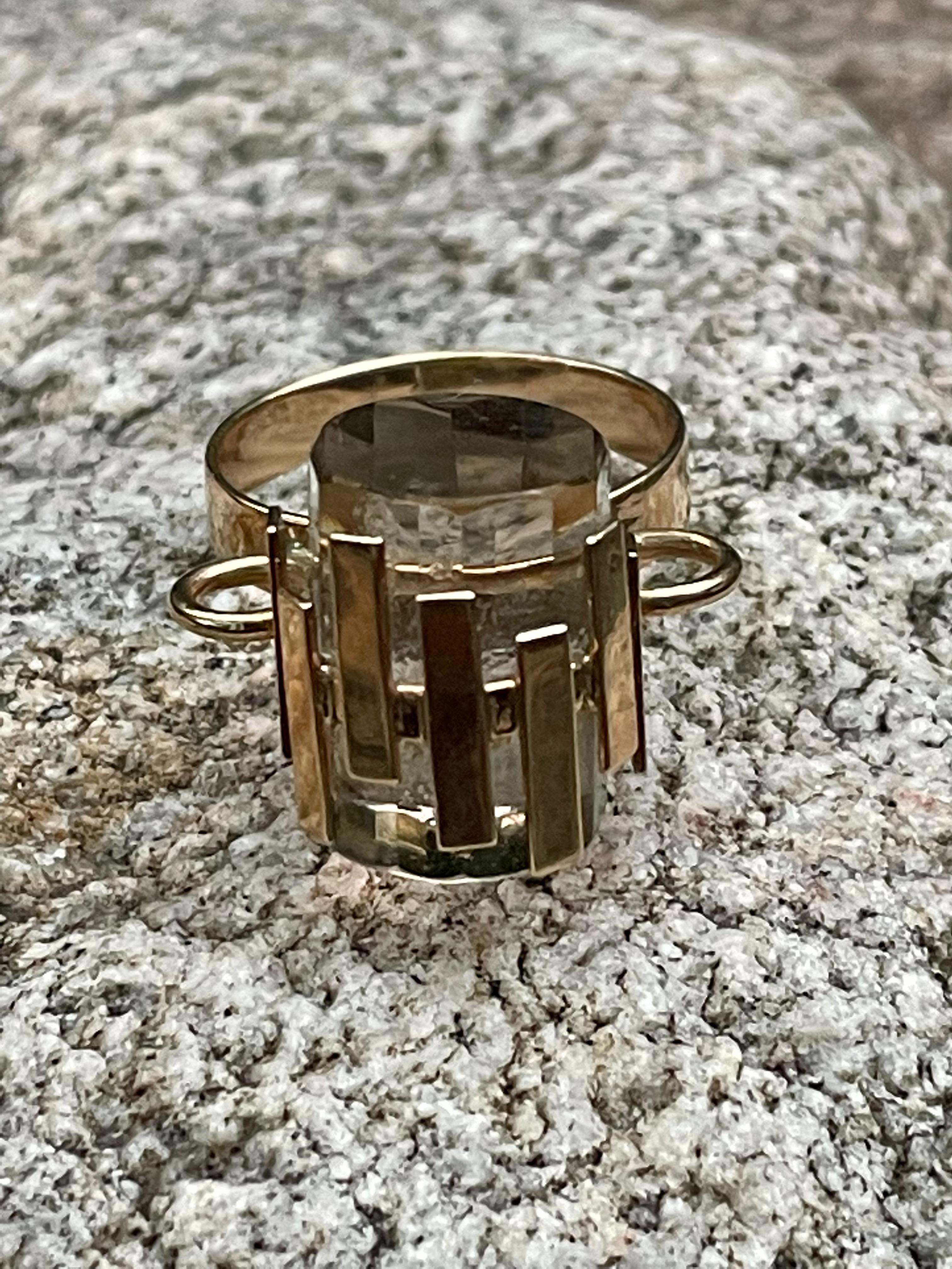 This unique fashion ring features a tube-shaped Smoky Quartz which measures 15 x 11mm.  It is mounted with a ring of 14 karat yellow Gold planks holding it in place and making it rise above the wearer's finger.  It's so unique.

Size: 7
This ring