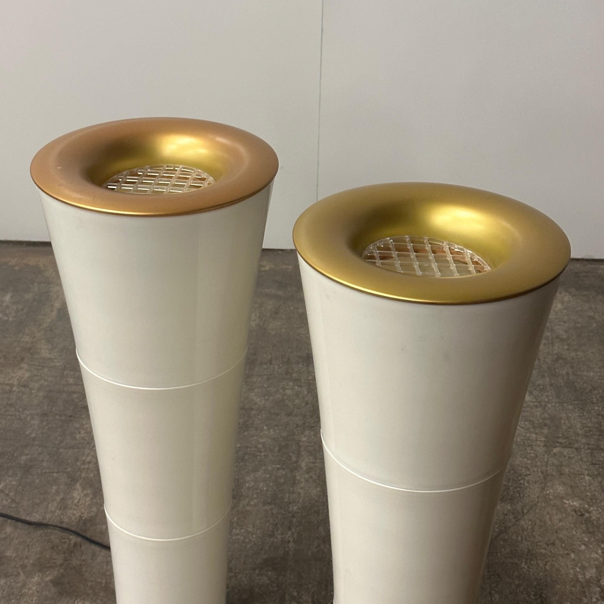These petite torchieres emit an up light and feature white plastic bodies with gold plastic around the top opening of the lamp. The opening is covered with a clear plastic grate. The pair feature the original push toe dimmer switches. Made in