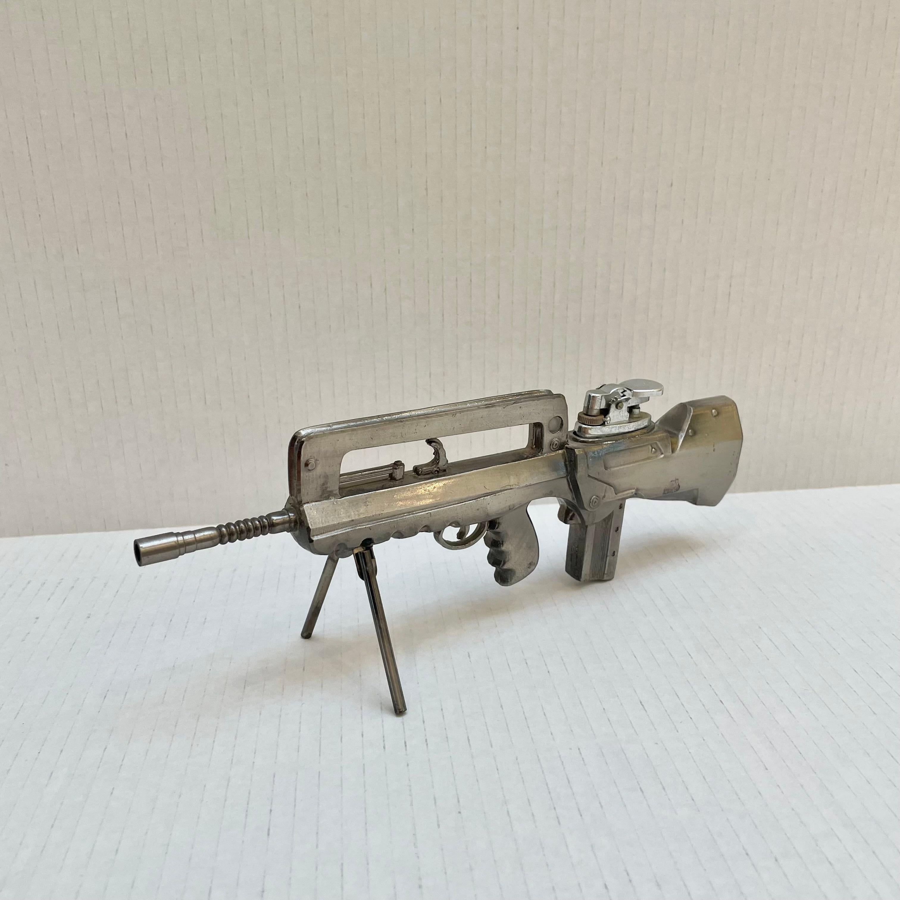 Cool vintage table lighter in the shape of a FAMAS (Fusil d'Assaut de la Manufacture d'Armes de Saint-Étienne) assault rifle. Made of metal and stands up on its own via bipod arms which can be folded up and down. Medium patina giving this piece a