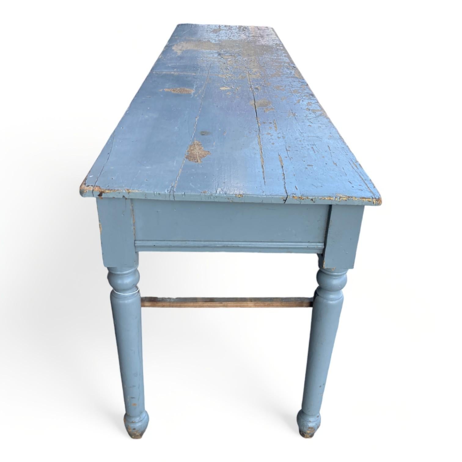 Our vintage farm console has a weathered surface with remnants of its original blue paint, creating a rustic and substantial statement piece. At 104