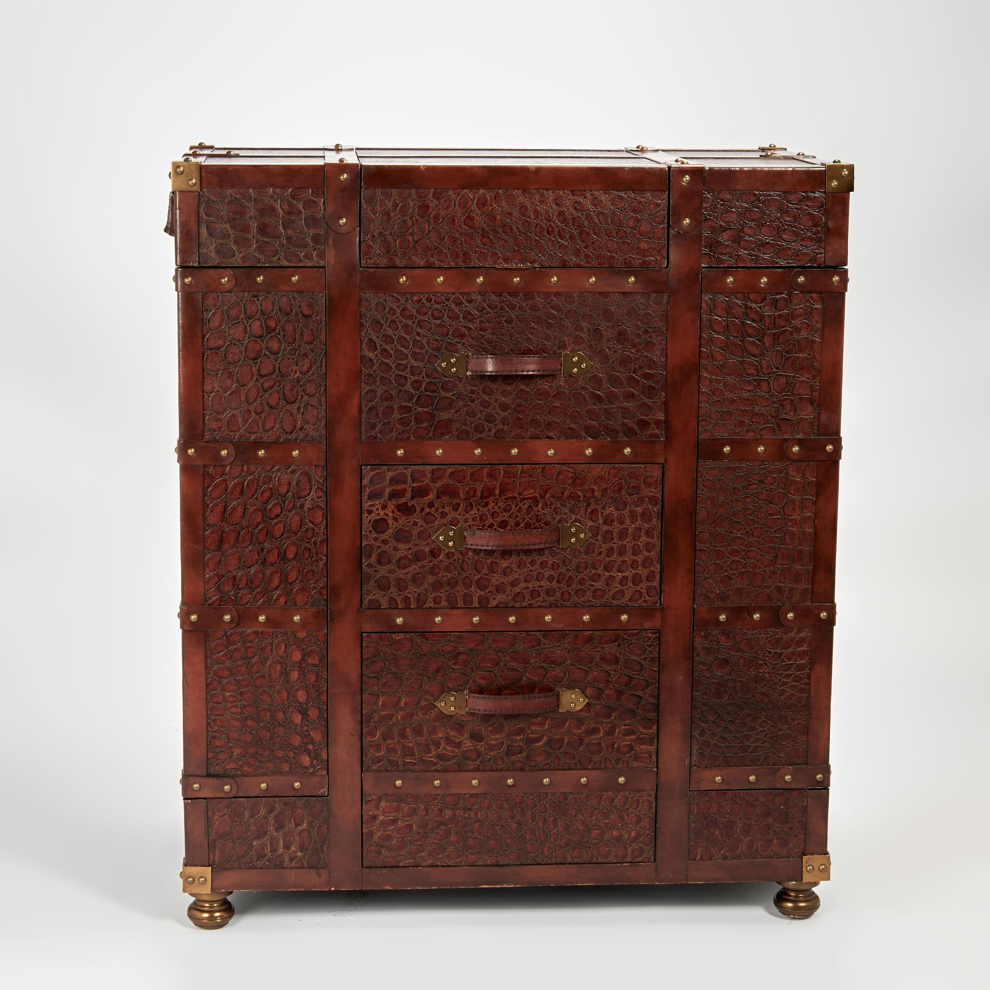 Dashing vintage steamer trunk clad in faux alligator leather with brown leather straps and brass tacks featuring a hidden bar with a mirror and stone top, bottle coolers, side cabinets for glasses and bottles and a lower drawer with a metal lined