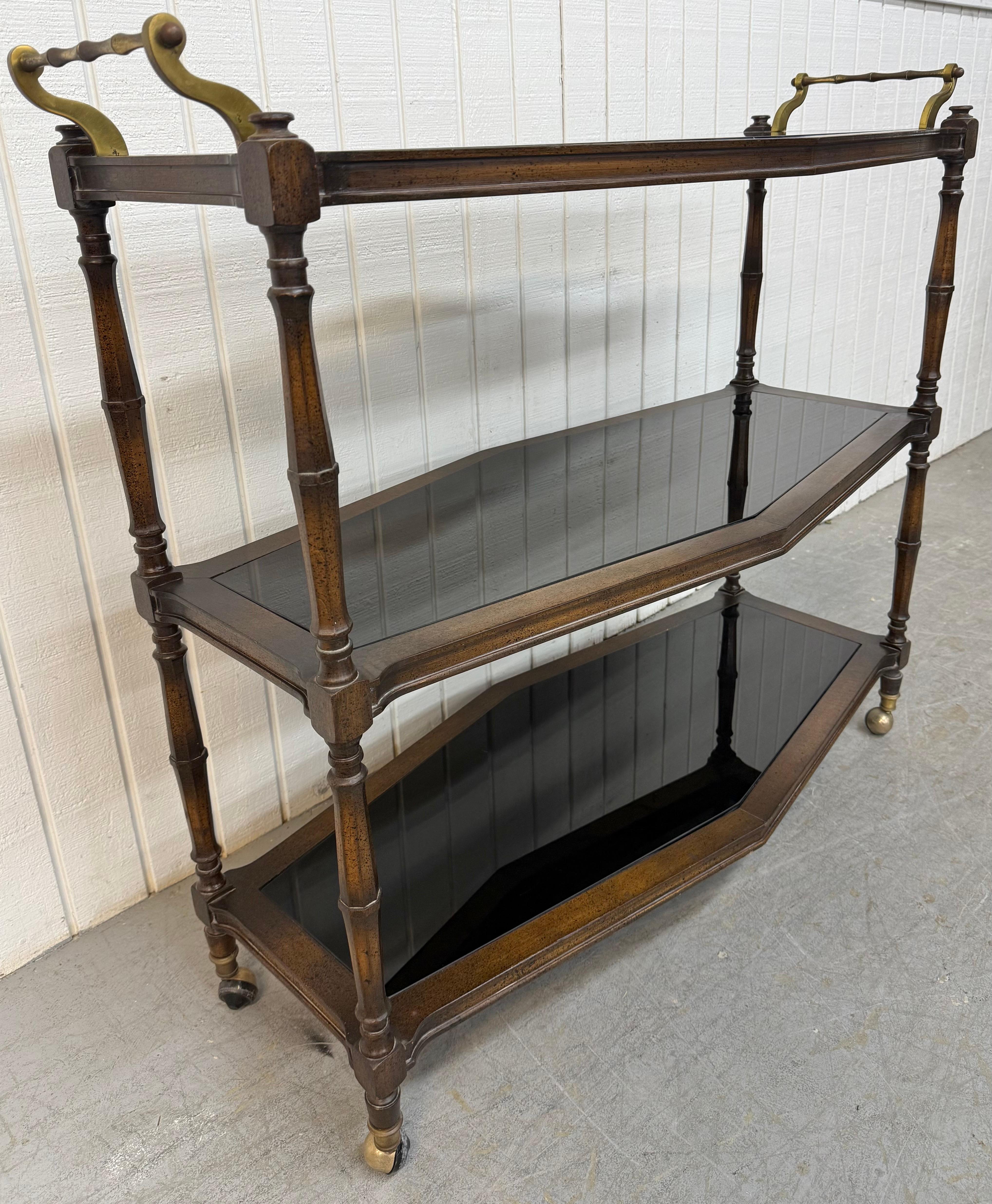 This listing is for a Vintage Faux Bamboo 3-Tier Smoked Glass Serving Cart. Featuring a solid wood faux bamboo frame, three tiers of smoked glass for storage, brass handles/wheels for easy transport, and a walnut finish. This is an exceptional