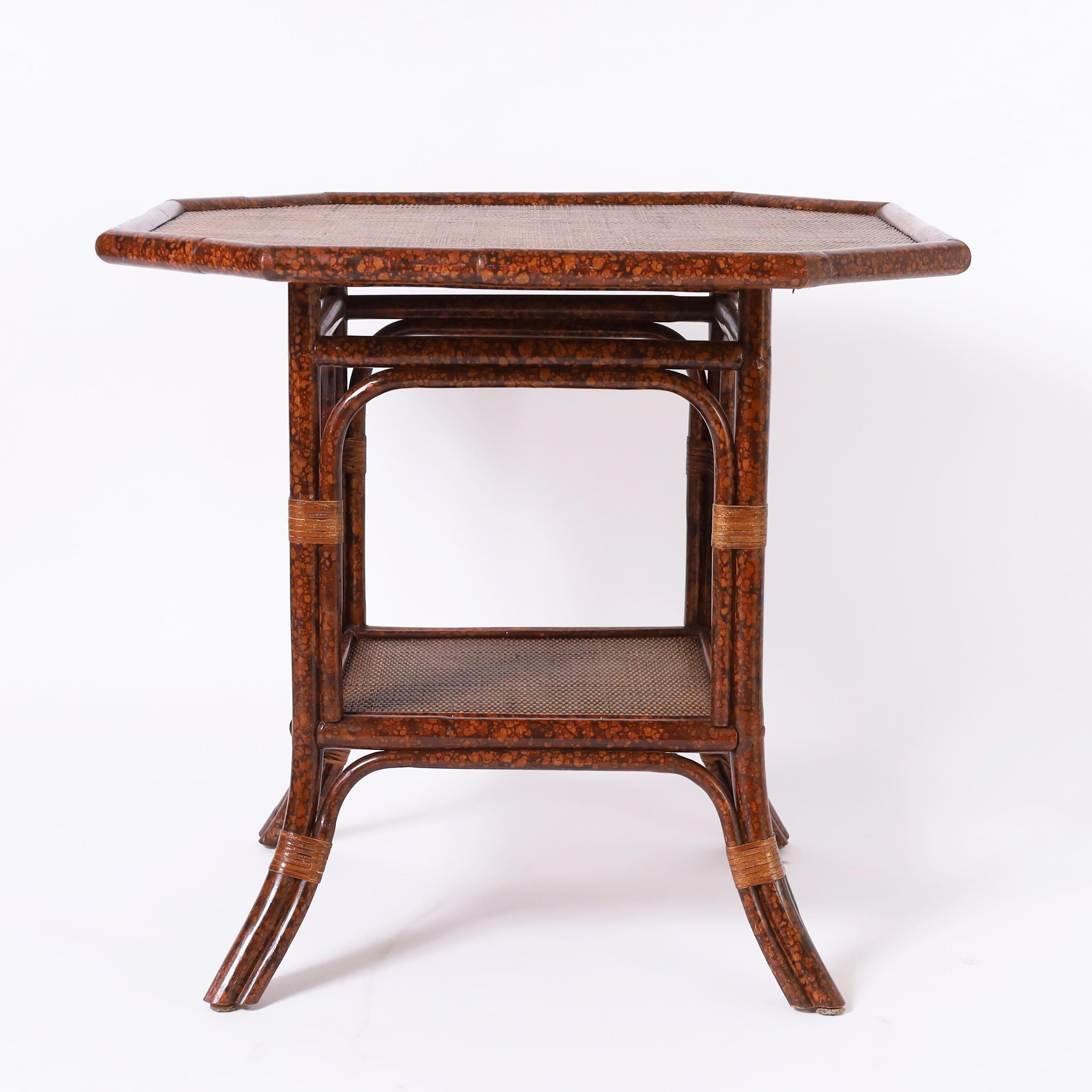 Magnifique table de style colonial britannique du milieu du siècle, fabriquée en faux bambou avec une finition en fausse tortue, avec un plateau de forme octogonale et un niveau inférieur recouvert d'une toile de gazon avec des touches enveloppées