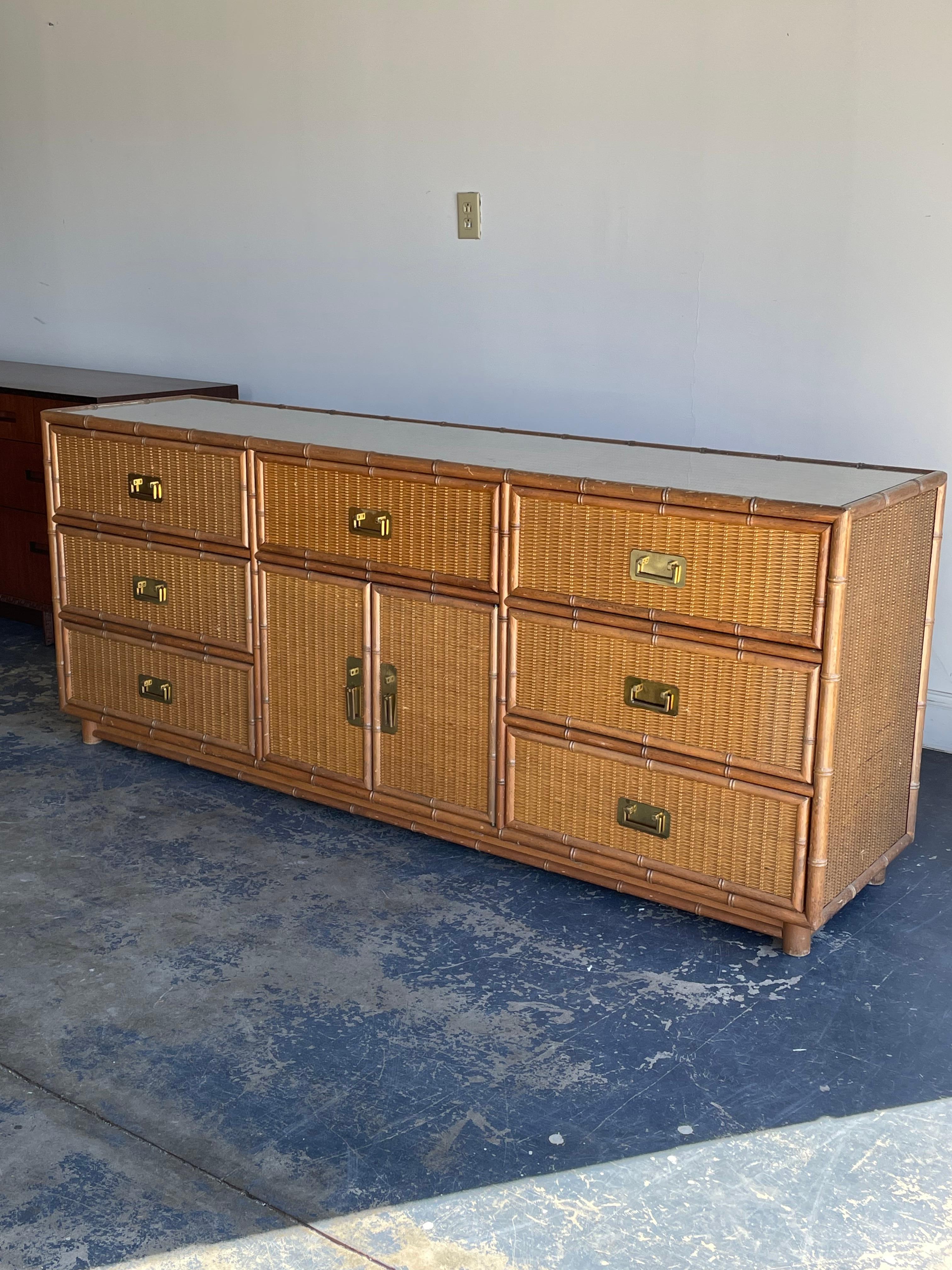 Vintage faux bamboo and rattan sideboard or dresser. Features bamboo framed case with rattan covered drawer fronts, sides, and top. Completed with brass hardware.