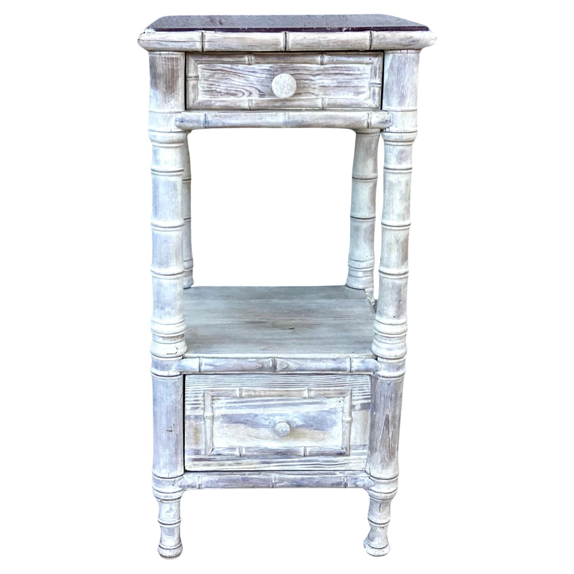 Charming vintage faux bamboo nightstand or side table with brown marble top. Table features a top drawer and a bottom shelf with door opening, and four turned post legs for support. Has a washed distressed finish for a well-worn patina to add to the