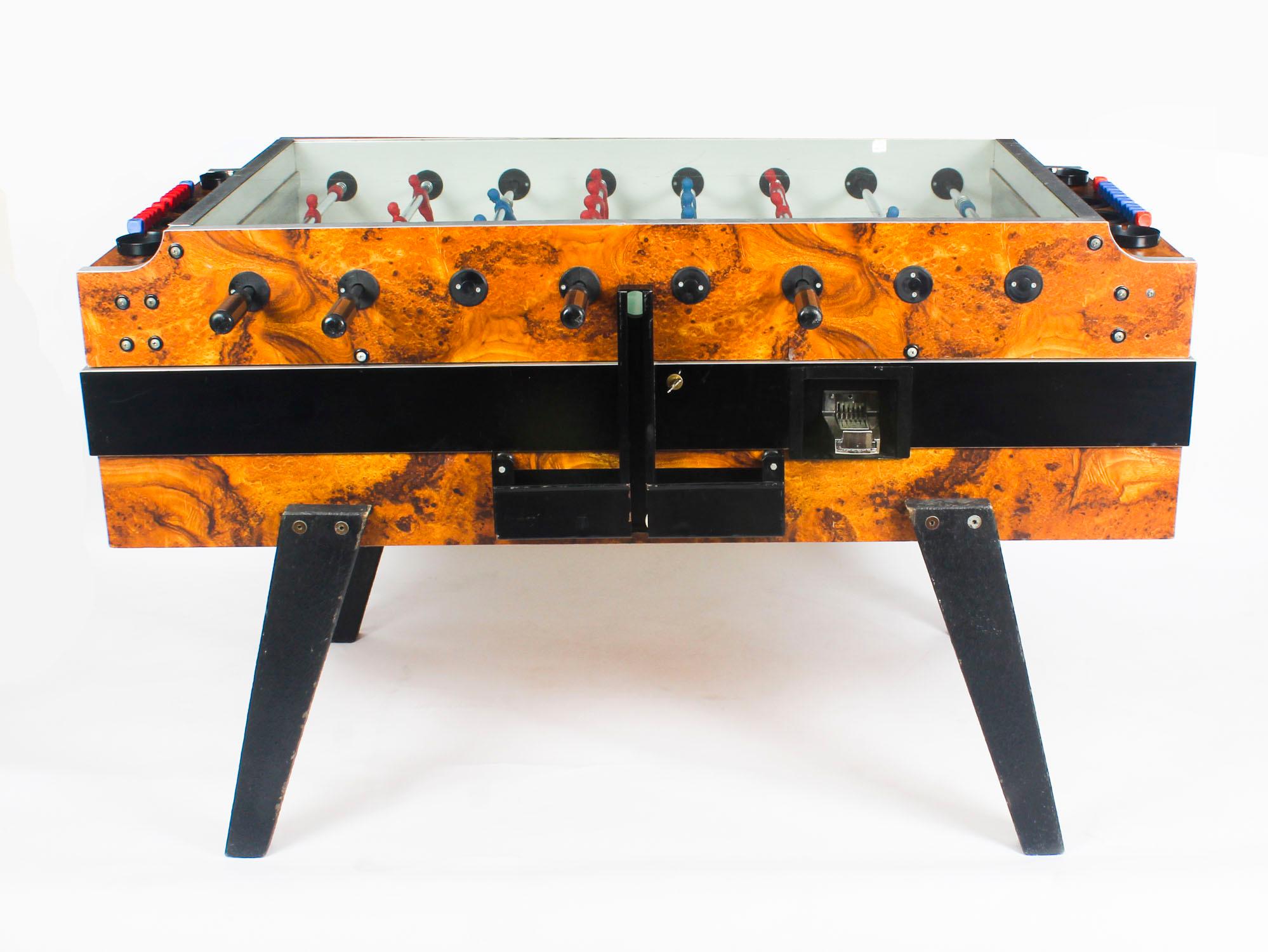 A vintage faux burr walnut football table, mid 20th Century.

The table features telescopic rods, toughened glass safety top, plastic handles with wood insert, ten balls and a sandblasted glass playing pitch. The table has solid wooden legs that