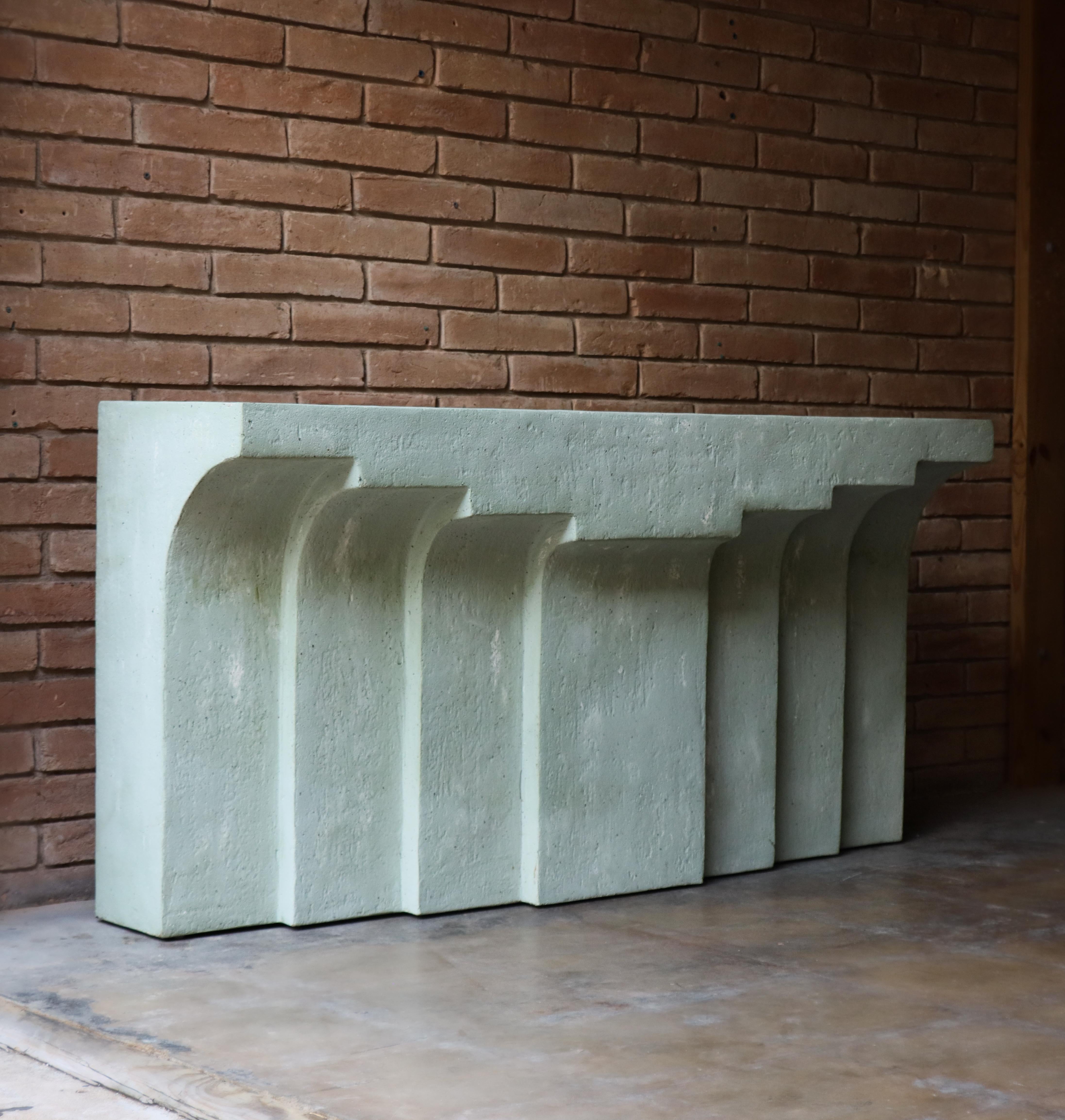 Unique modernist faux concrete console table. Features a beautiful pale sea foam or mossy green textured color. 

Fiberglass construction with textured surface to resemble cast concrete. Stepped modern arched design. The console is finished on all