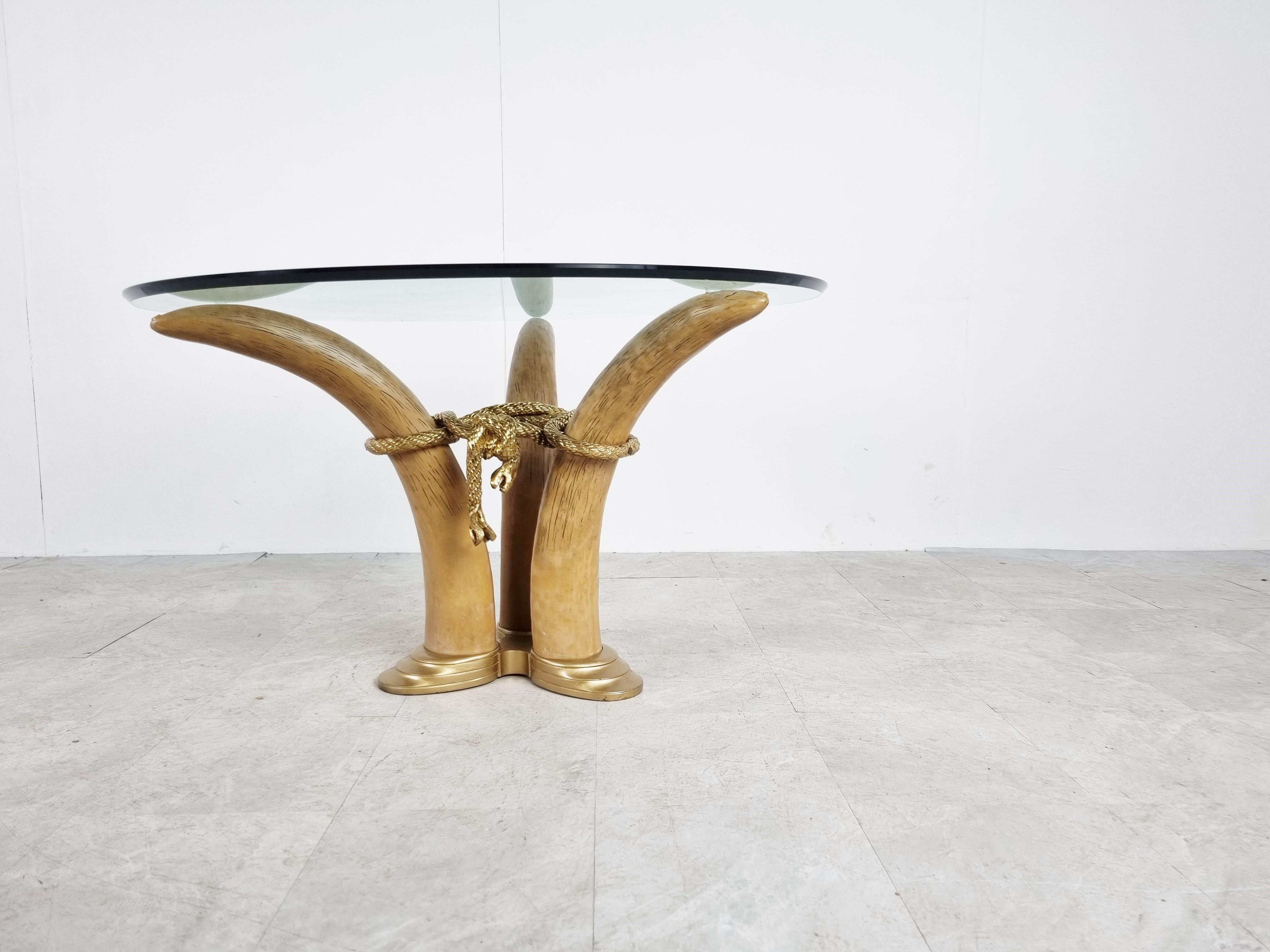 Elegant center table featuring faux elephant tusks made from resin mounted on a metal base with a round beveled glass top.

Real eye catching piece.

The standard height might be a bit low for a dining table, it can also be used as a coffee