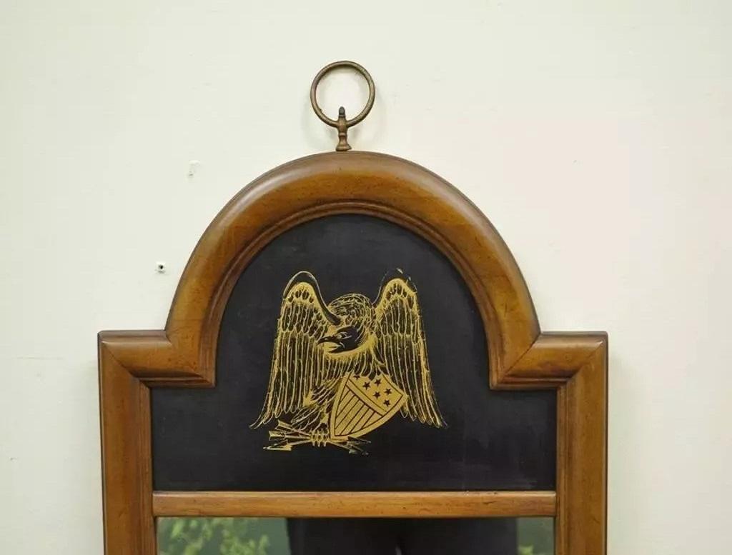 Miroir mural vintage à cadre étroit en cerisier, de style Feder, avec aigle en or. L'objet présente un écusson en bois peint en noir, un aigle américain doré et un bouclier. Circa Mid 20th Century. Dimensions : 49