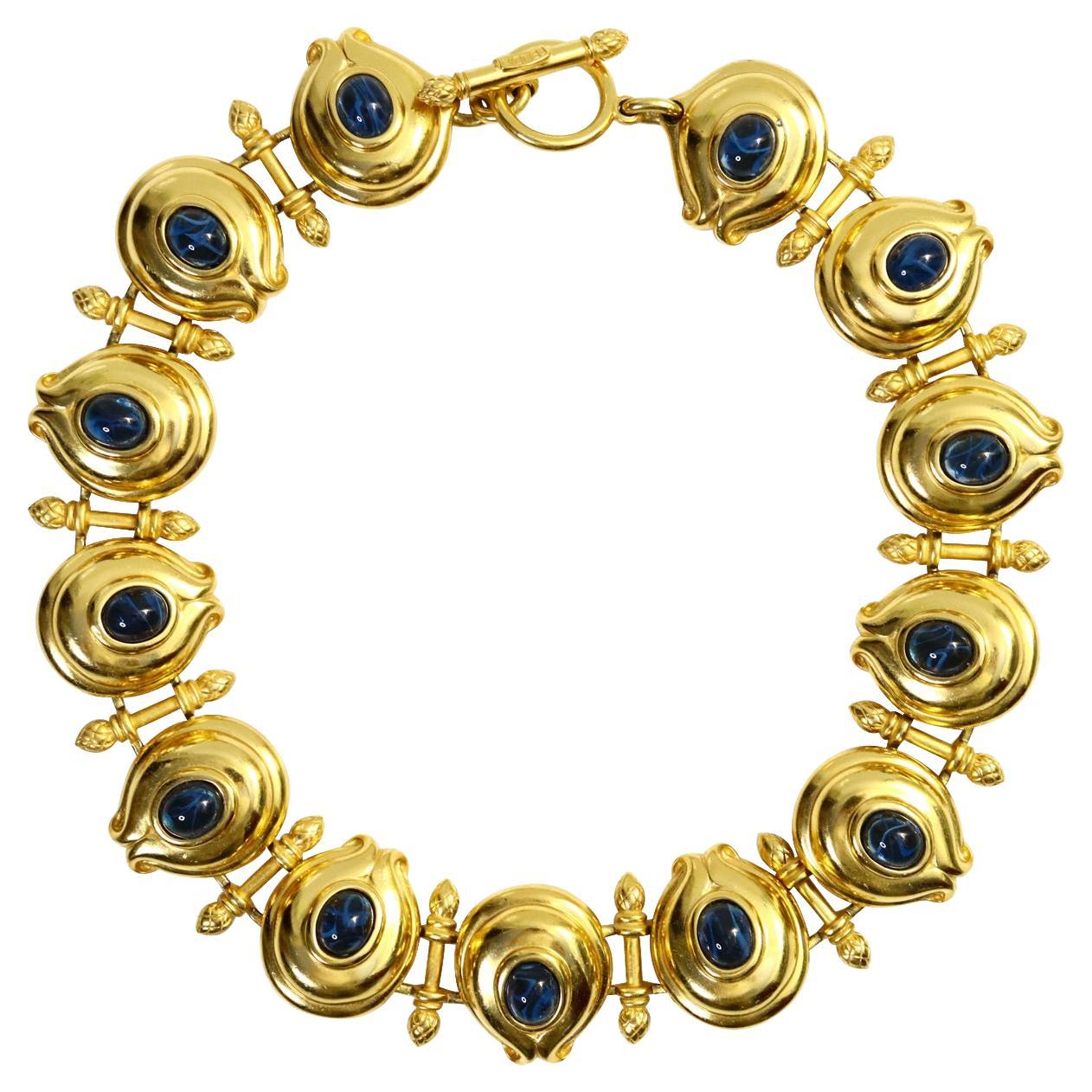 Vintage Fendi Gold-Ton und Blau Cabochon Toggle Halskette. Eine umfangreiche Halskette aus den 1980er Jahren besteht aus ovalen Goldscheiben mit blauen, glänzenden Cabochons und einer Kugel mit einem Weizenmuster, die jede Scheibe trennt. Am Ende