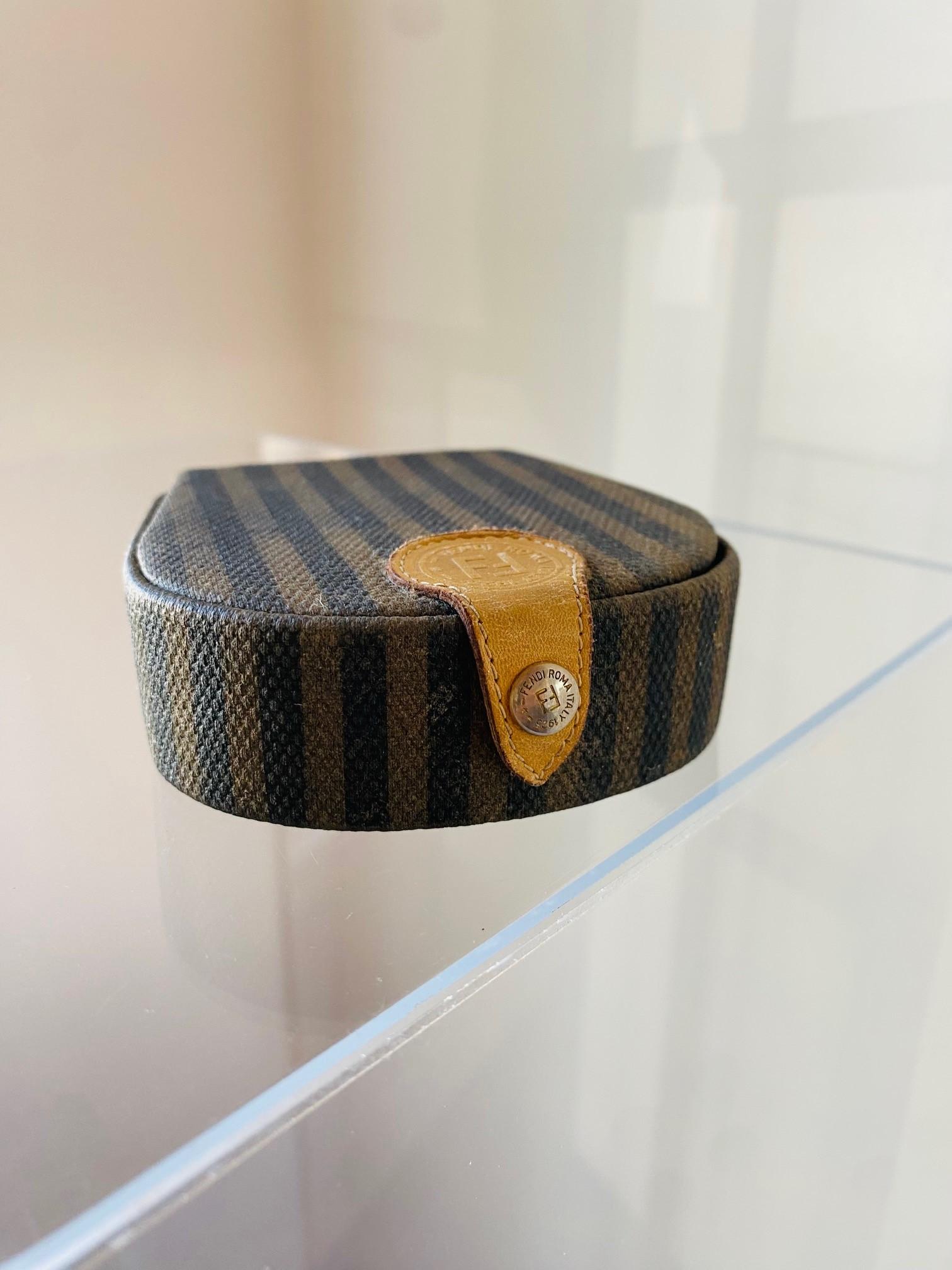Unique and interesting trinket box by Fendi.  This vintage piece from the early 1990s is made in leather and covered in the classic Fendi Pequin stripe fabric design.  This piece opens with a snap hardware button that holds the Fendi logo to reveal