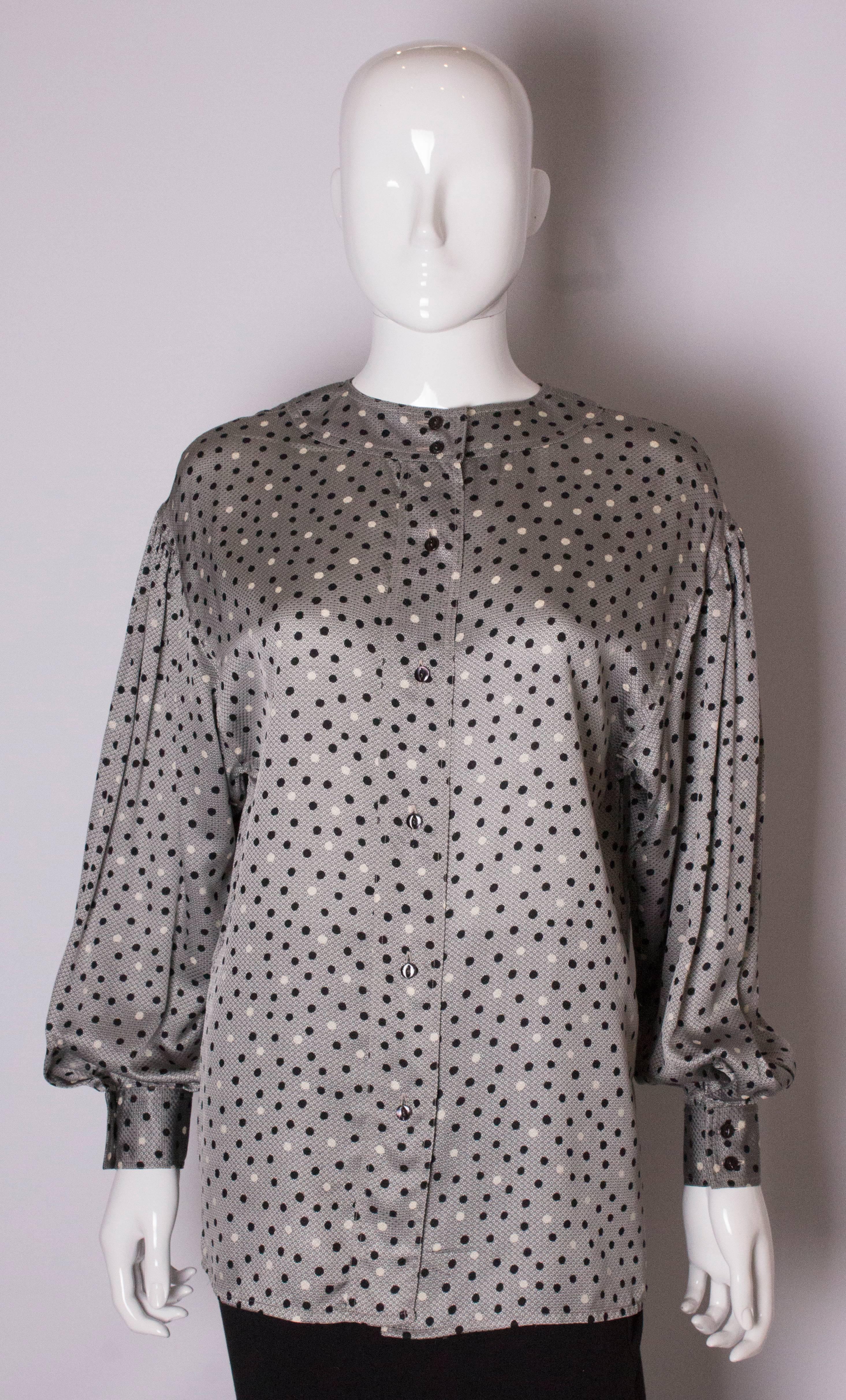 A chic vintage blouse by Ferragamo. The blouse has a grey silk background and black and white spot detail, with 2 button cuffs , round neckline and button opening at the back, with foldovers at the front.