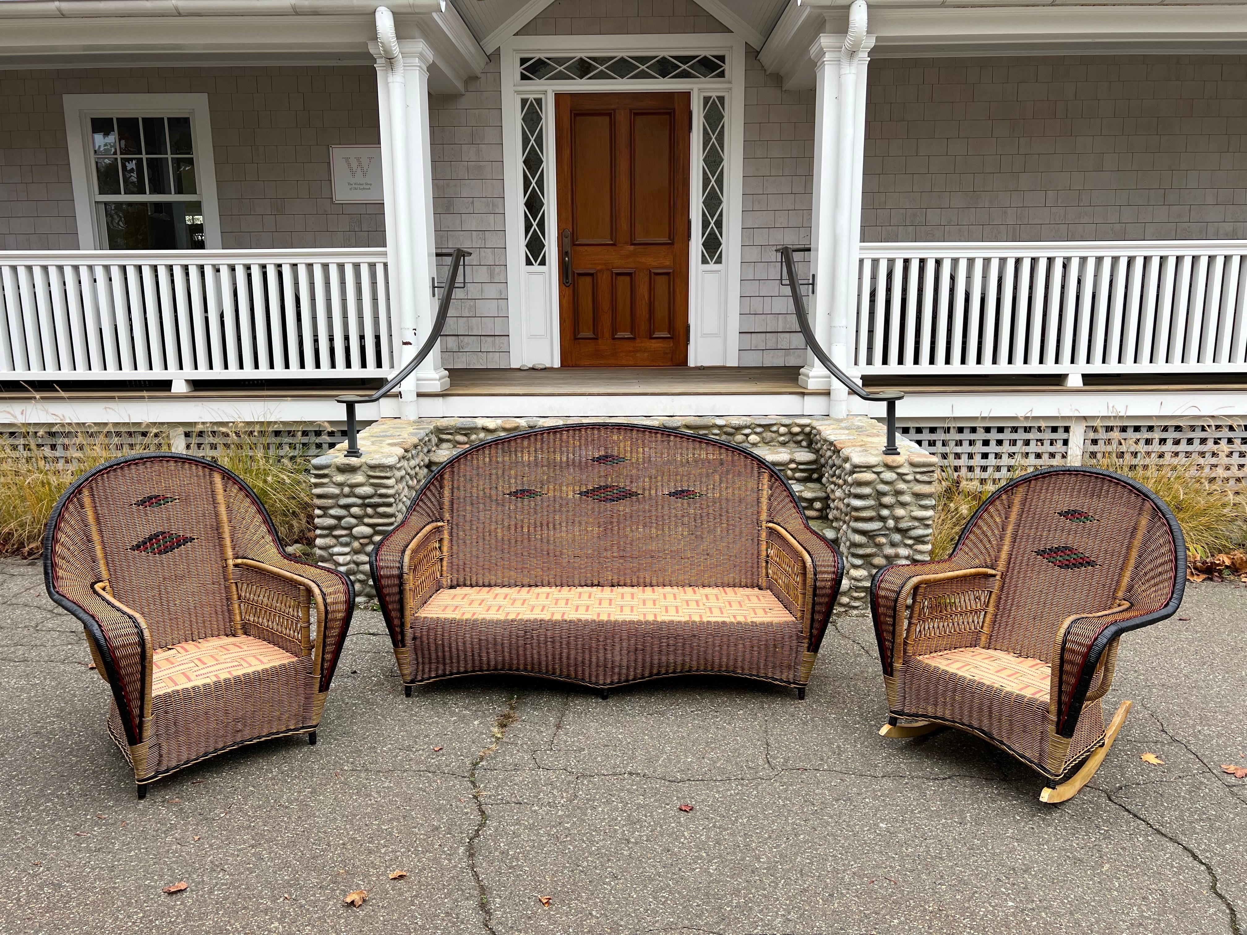 A beautiful antique wicker set by Ficks Reed. Woven of reed with an overall natural stain, the pieces have red, green and black painted highlights and trim. New decking covers spring seats. This set has been cleaned and sealed and minor breaks have