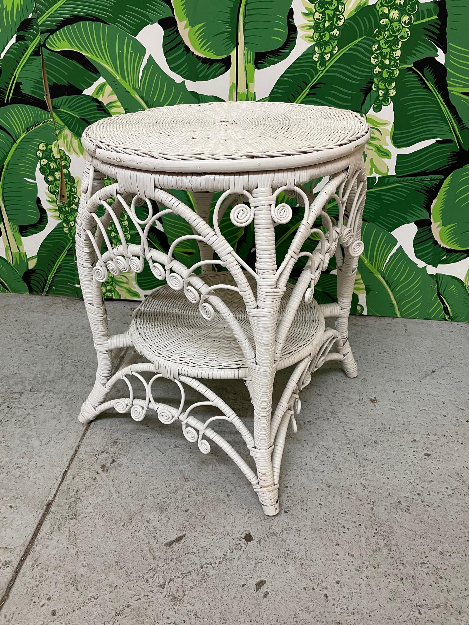 Vintage fiddlehead wicker side/end table features woven top and ornate scrolled and filigree aprons. Rattan wrapped frame and splayed legs. In the manner of Heywood-Wakefield. Good condition with imperfections consistent with age, see photos for