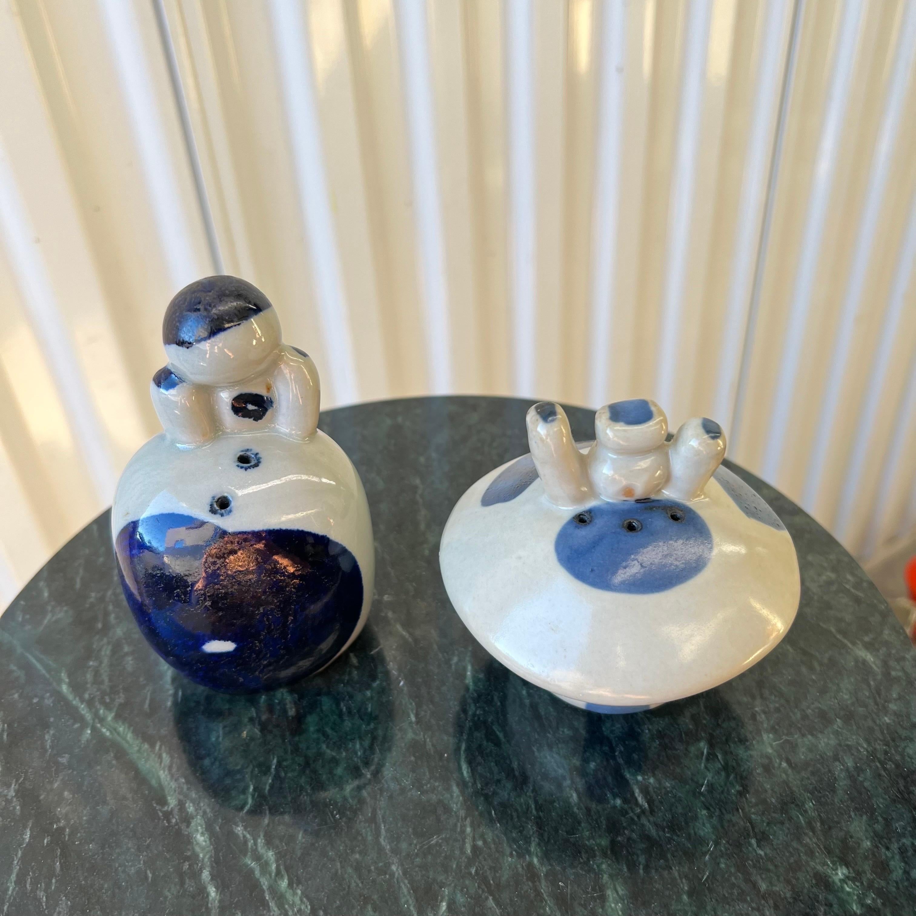 A funky set of glazed stoneware figurative salt and pepper shakers in blue and white delft style.  
The pepper shaker (the taller one) measures: 4.75” tall x 2.75” wide x 2” deep.  The salt shaker measures: 3.75” tall  x 4” diameter