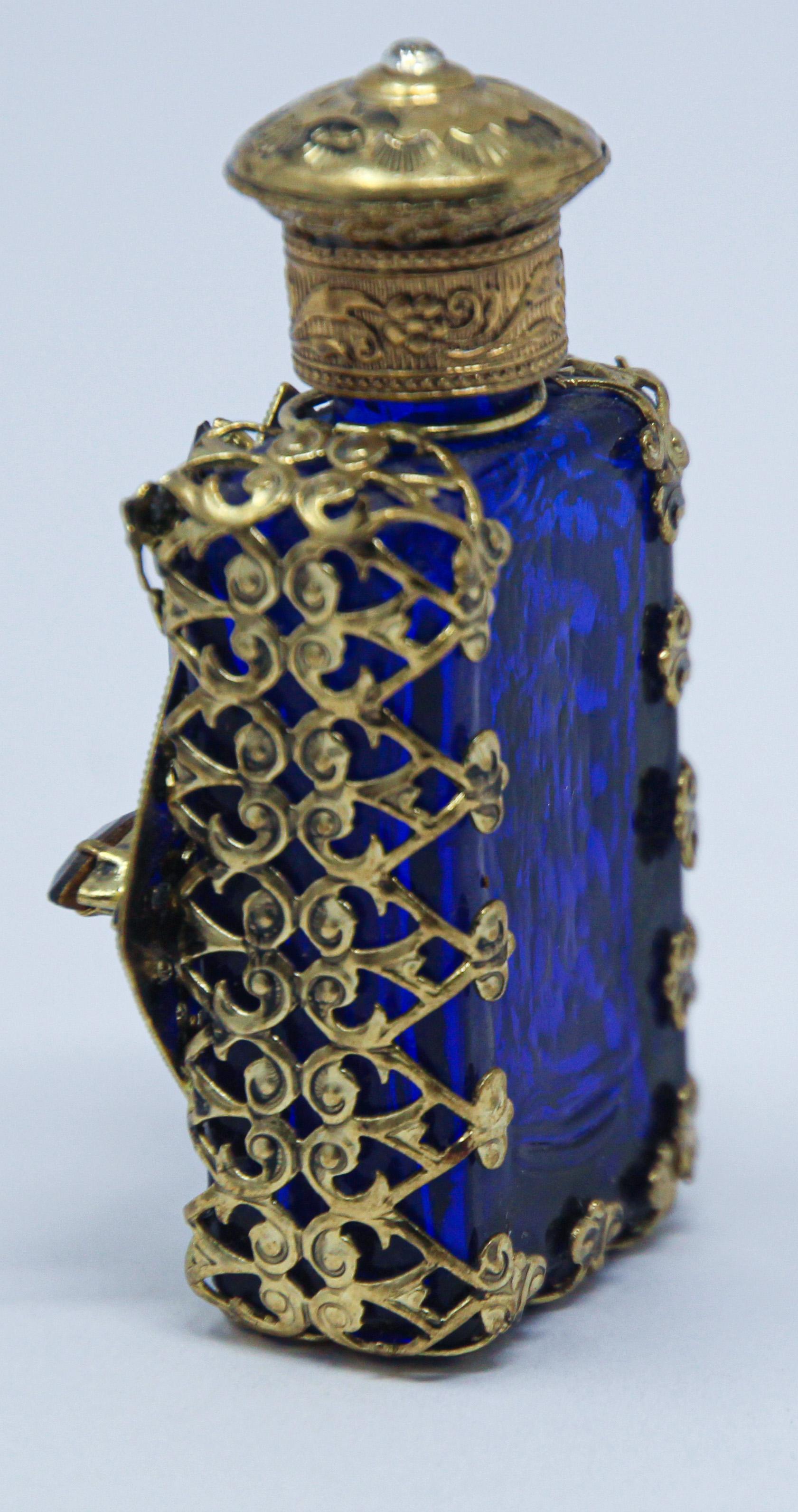 Pressed blue glass perfume bottle with a jeweled filigree sleeve.
Hollywood Regency pressed glass vanity perfume bottle with stopper.
The bottle features an ornate gold toned filigree collar and front panel with small inlaid beads of colored