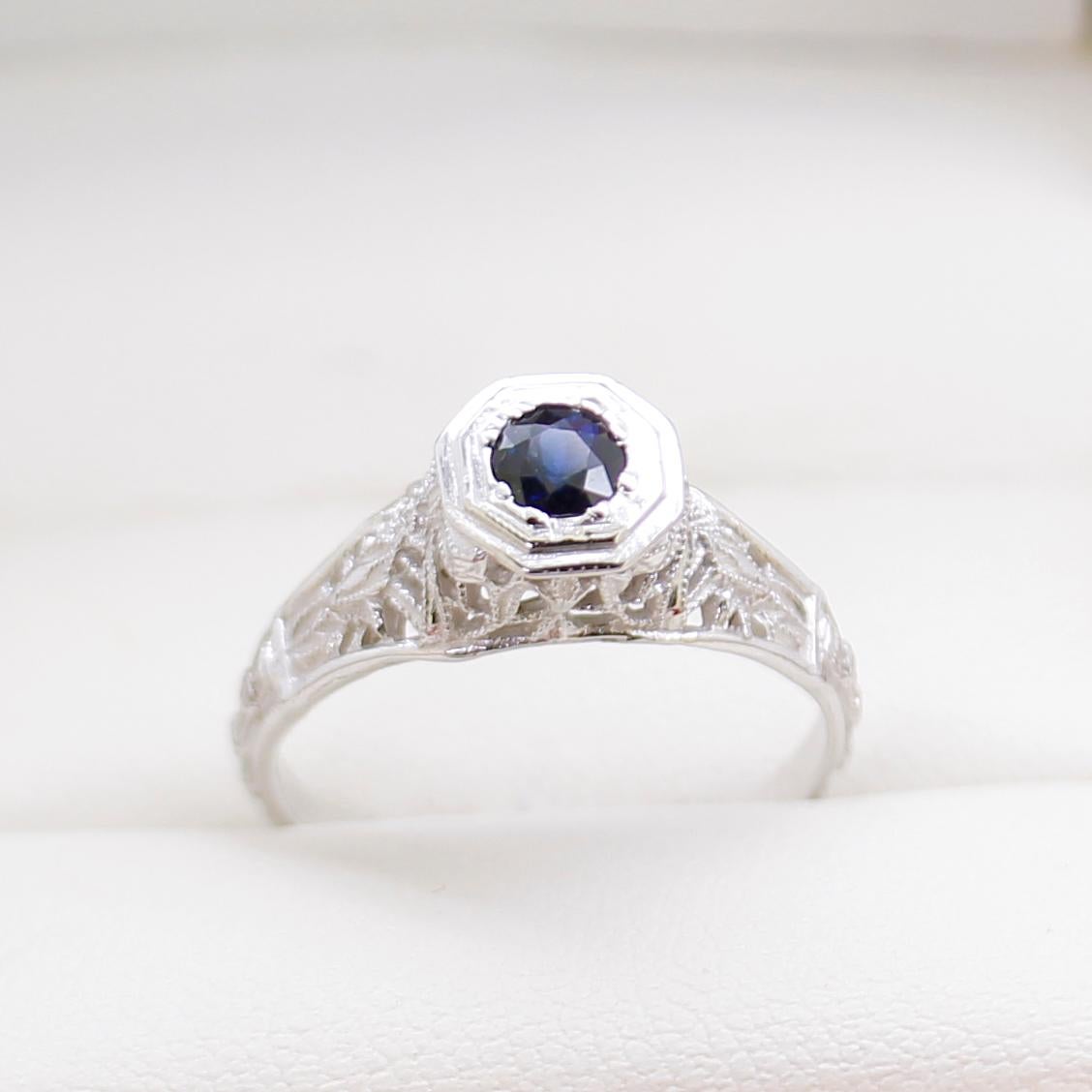 14ct White Gold Ring, narrow, low half round, tapered shank with open back polished finish, stamped (14K).

The Ring Contains:

One claw set round natural blue sapphire, colour is 