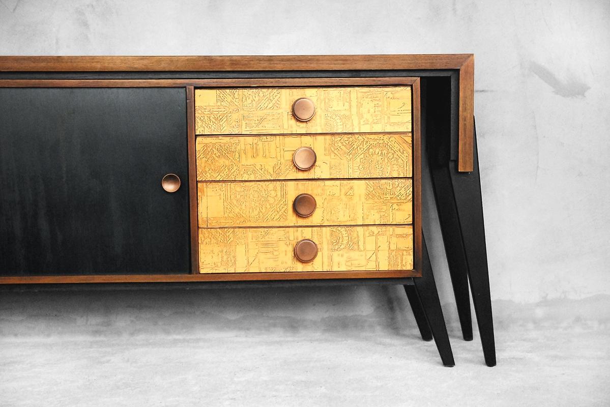 This modern sideboard with a desk top was manufactured in Finland during the 1950s. It is made from walnut wood and veneer. The sideboard features a pair of sliding doors in black and four drawers with original copper reliefs. The push-close desk is