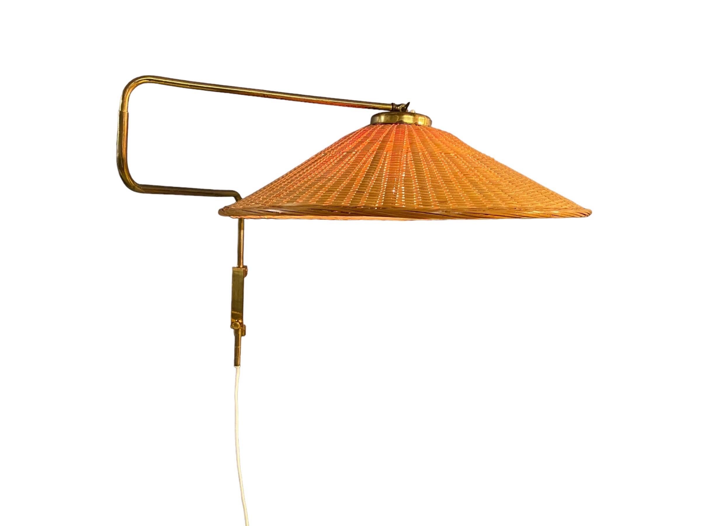 Lampada da parete vintage in ottone e vimini/rattan prodotta da Valinte in Finlandia negli anni Cinquanta. La lampada presenta uno stelo in ottone con un meccanismo regolabile che permette di proiettare la luce in quasi tutte le direzioni. L'ottone