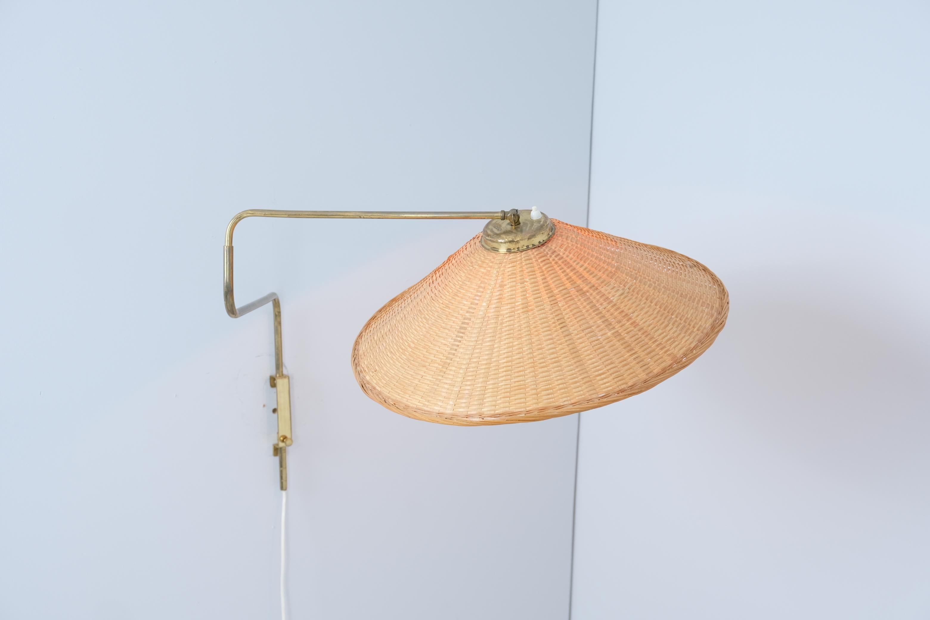 Aplique vintage de latón y mimbre/ratán fabricado por Valinte en Finlandia en la década de 1950. La lámpara tiene un vástago de latón con un mecanismo ajustable que permite proyectar la luz en casi cualquier dirección. El latón y el ratán se