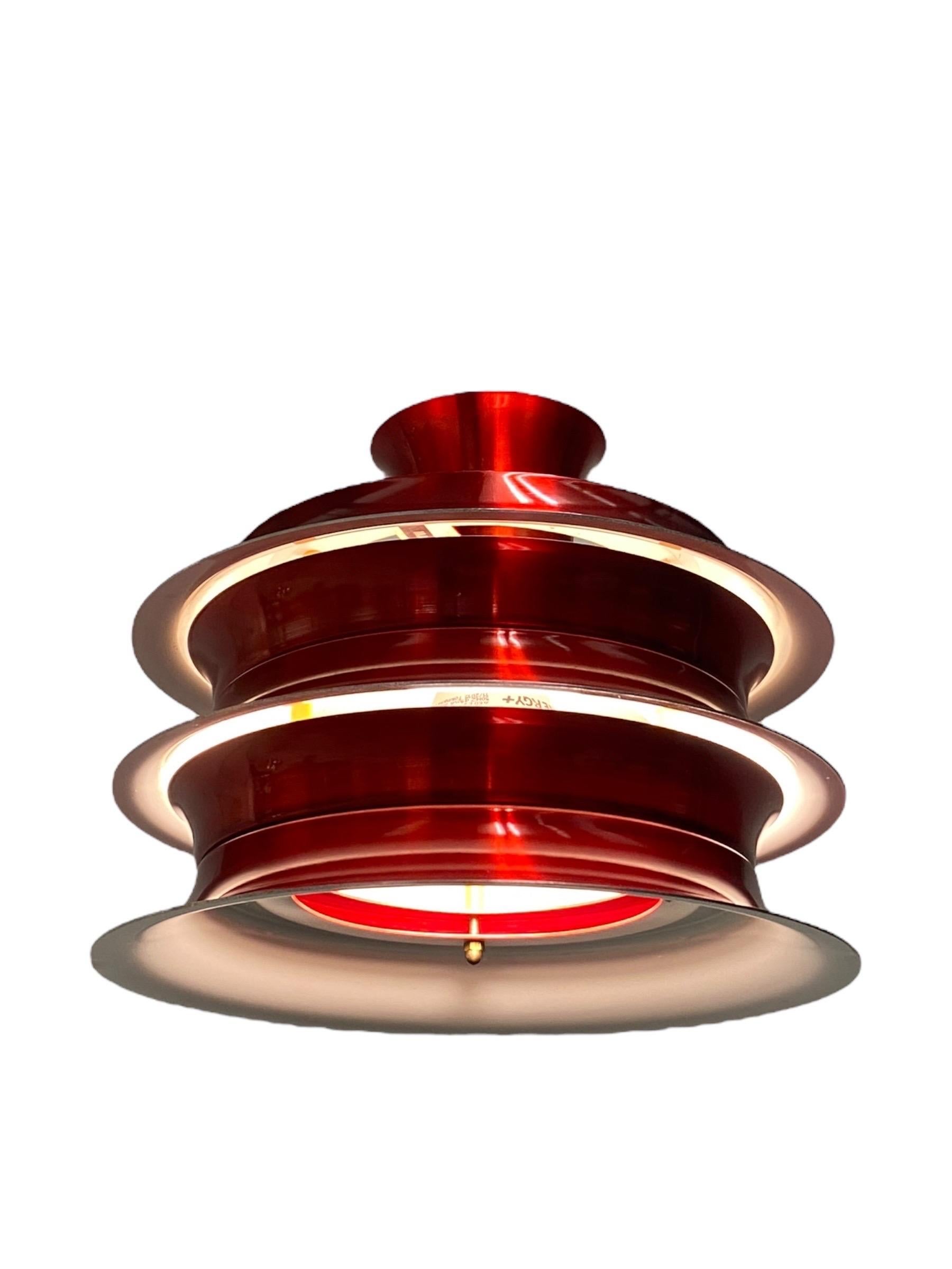 Questa lampada a sospensione vintage scandinava della metà del secolo scorso sfoggia un iconico design a strati con un'audace finitura rossa lucida. La lampada è composta da una serie di paralumi circolari in metallo impilati con leggeri spazi vuoti